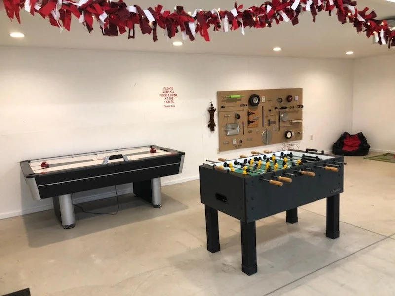 A view of the side area in the rec center, which shows some hanging garland, an air hockey table & a foosball table