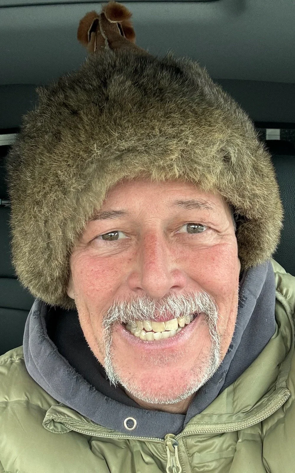 A white man in his 50s smiling and wearing a fur hat