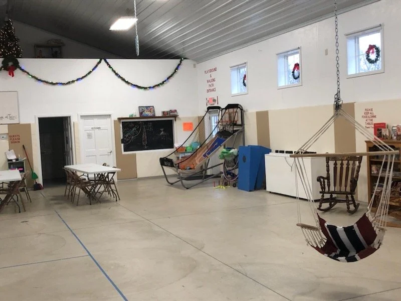 The indoor space, which includes a view of the basketball hoops, tables, miscellaneous music equipment, a swing and more.