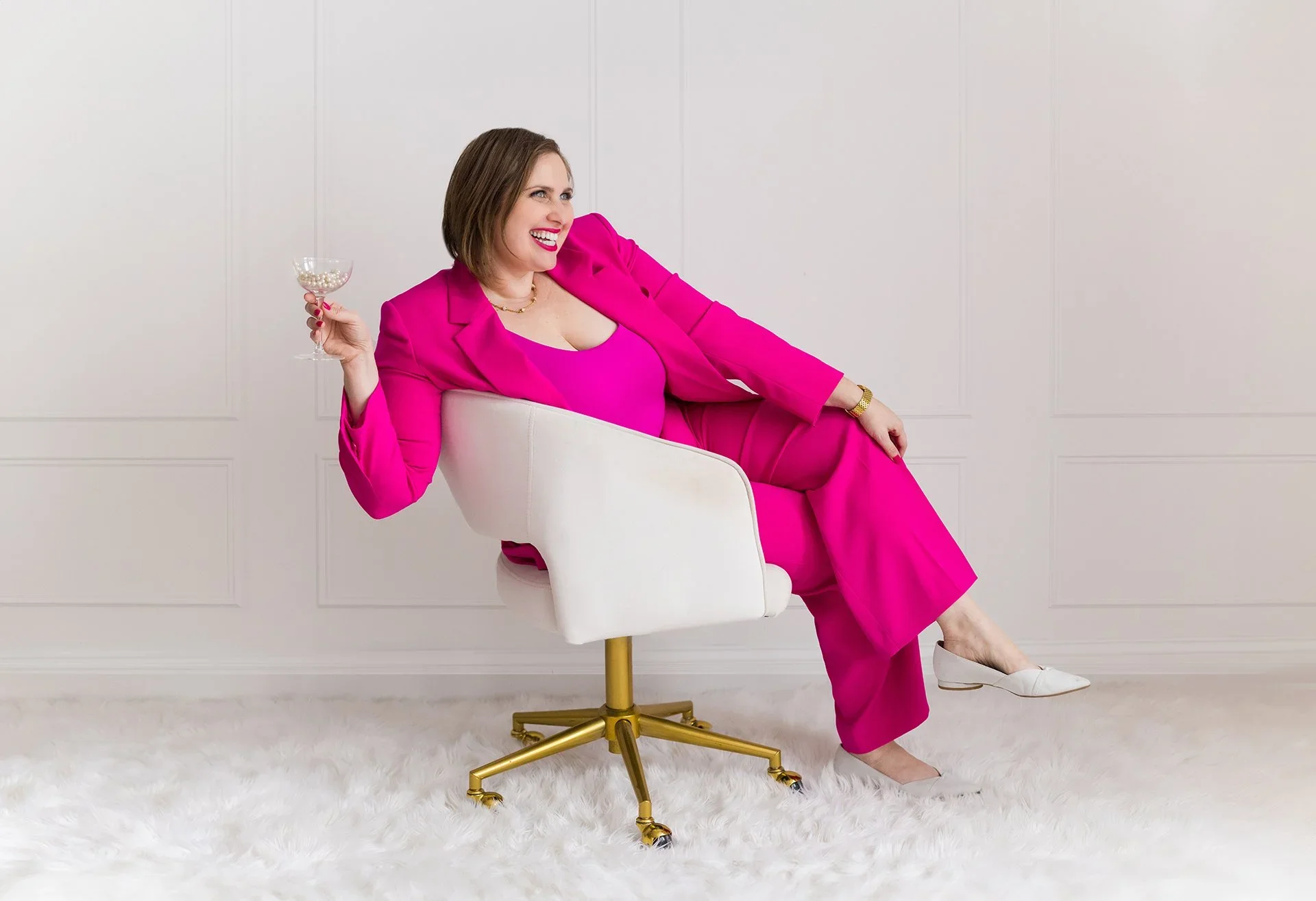 A woman sitting at a wooden desk working on a laptop, with a newspaper and a smartphone beside her.