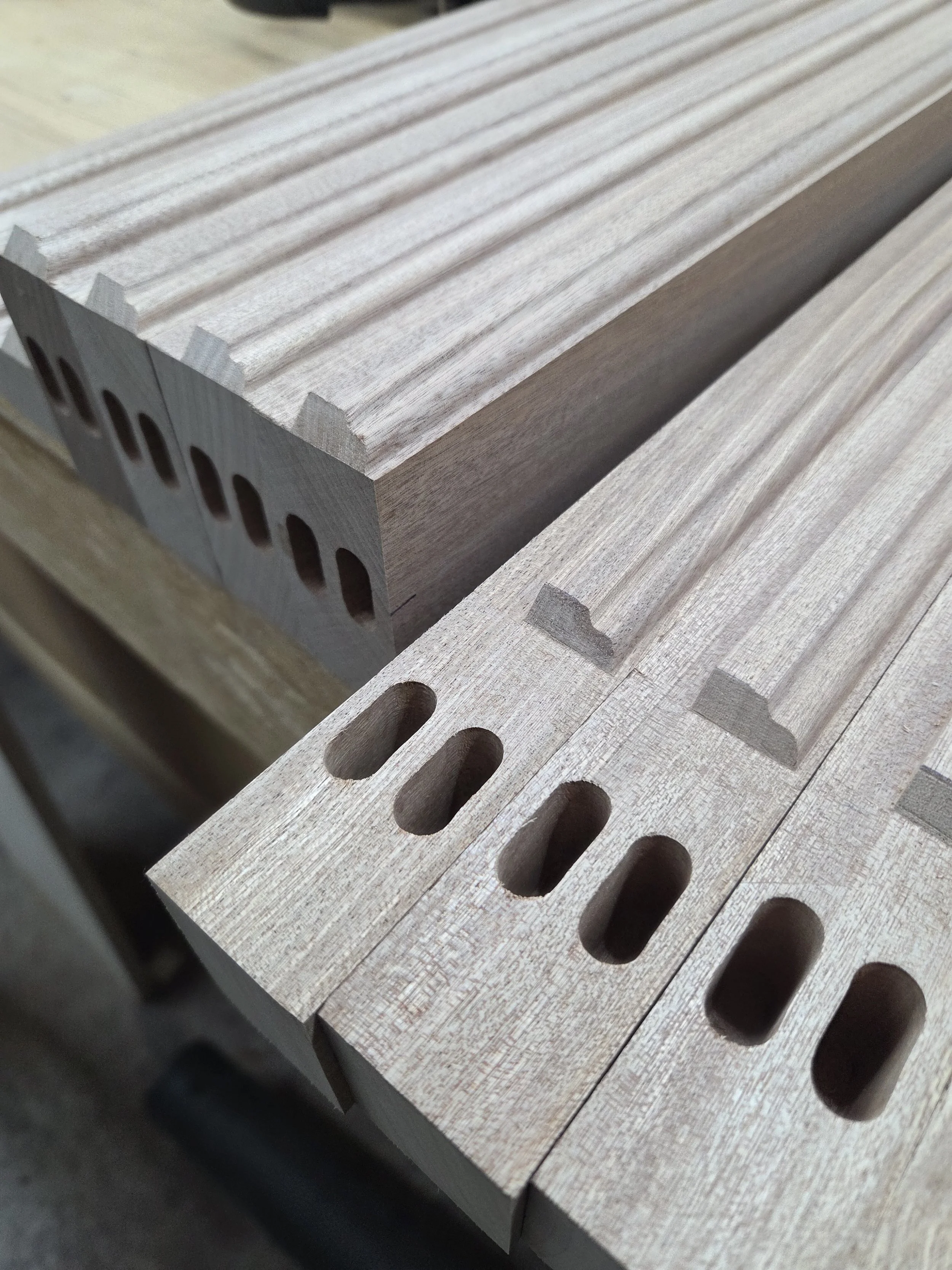 Close-up of several pieces of light-colored wood with elongated oval holes drilled into each piece, arranged on a surface.