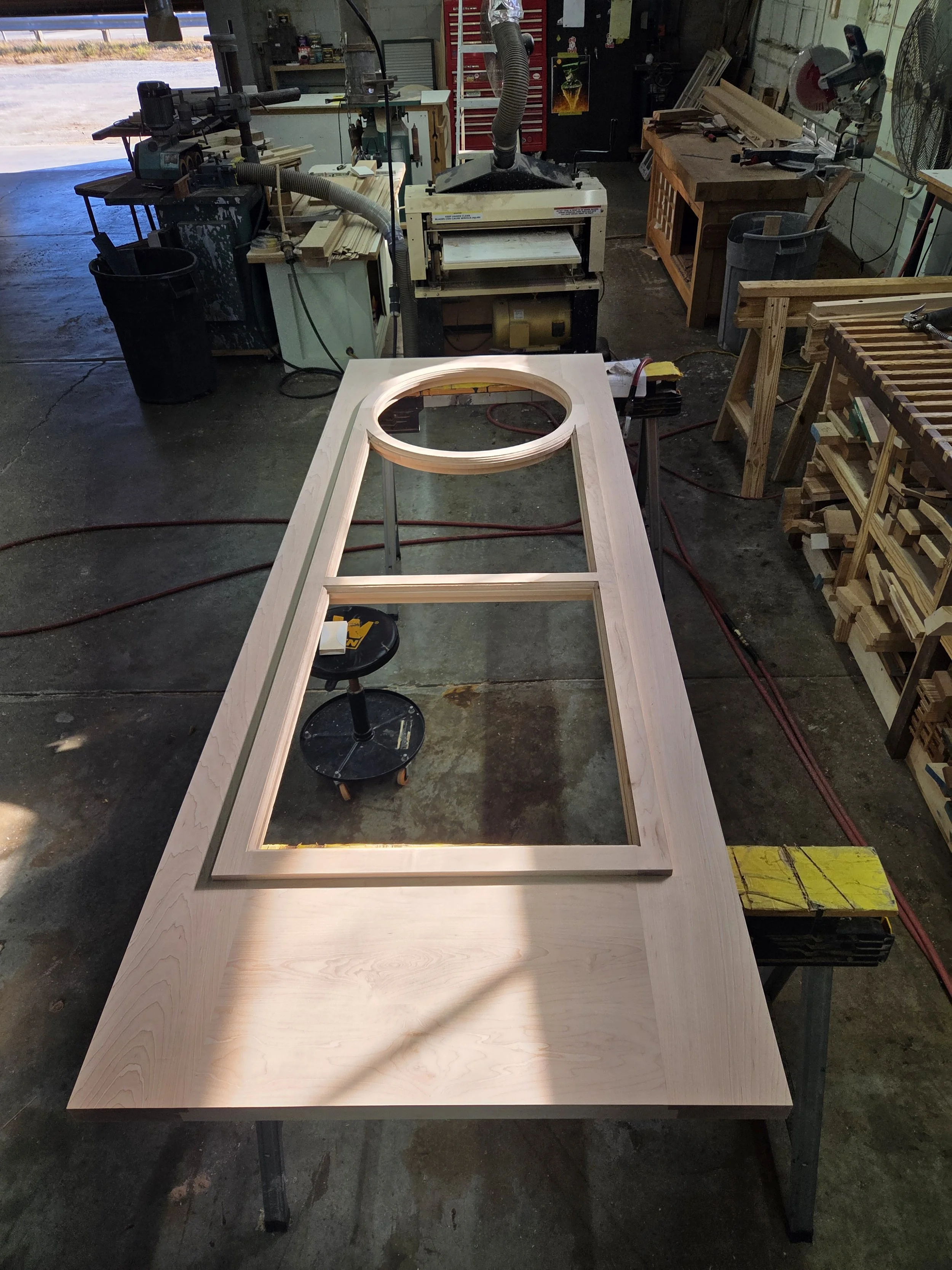 A woodworking workshop with a large wooden frame and a circular cutout in the center, surrounded by various tools and equipment.