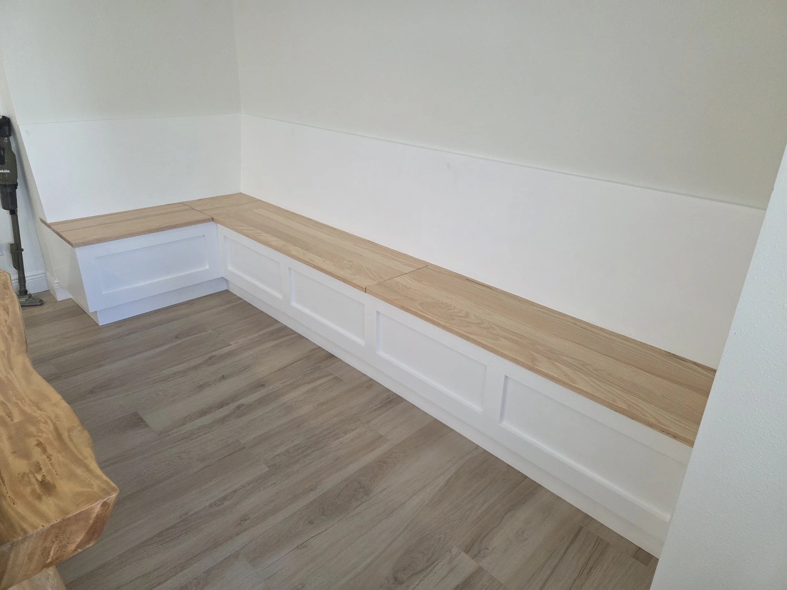 Built-in wooden bench with white cabinetry underneath, against a white wall.