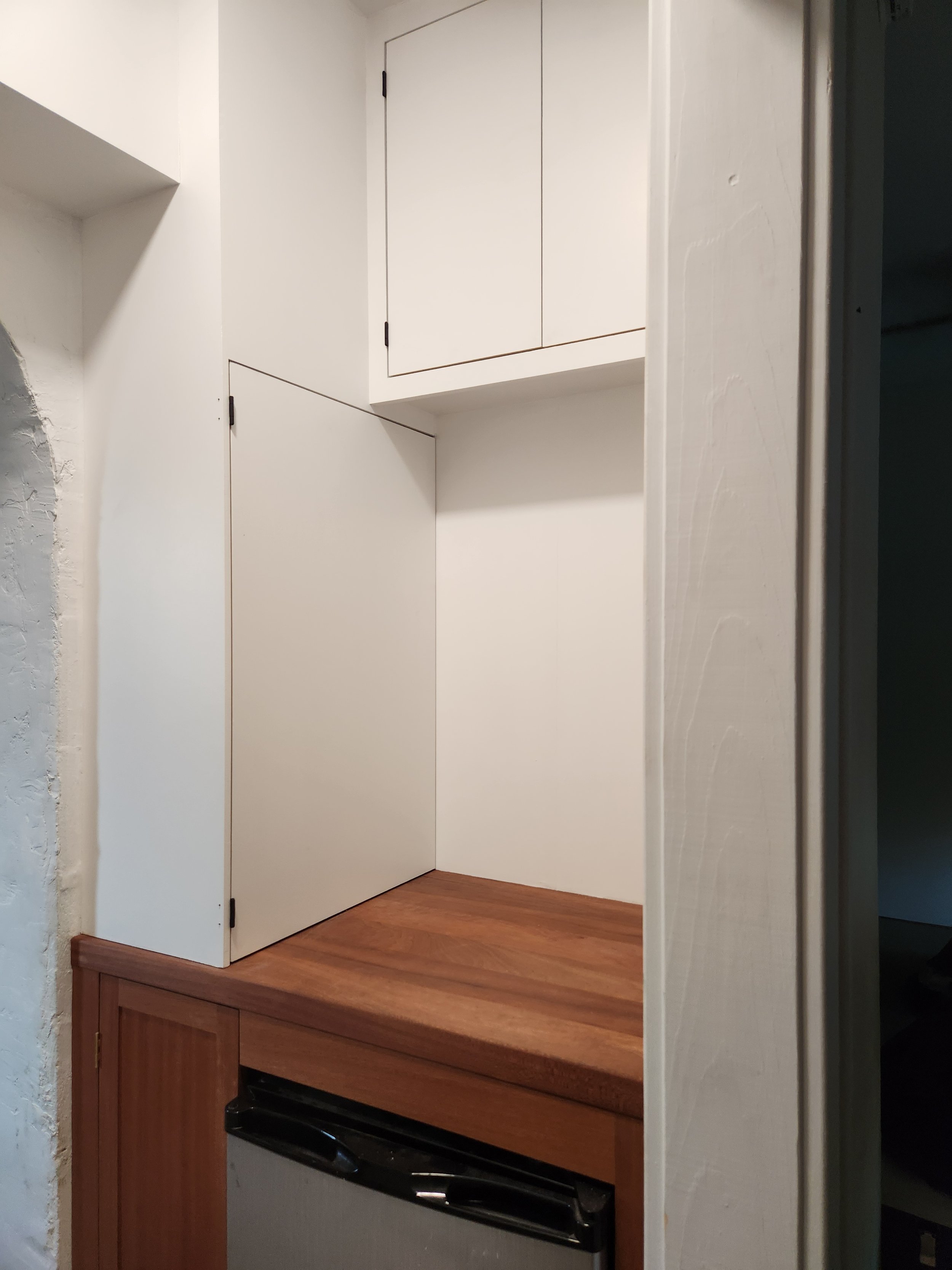 Interior of a kitchen with a wooden countertop, a white wall, and white cabinets above.
