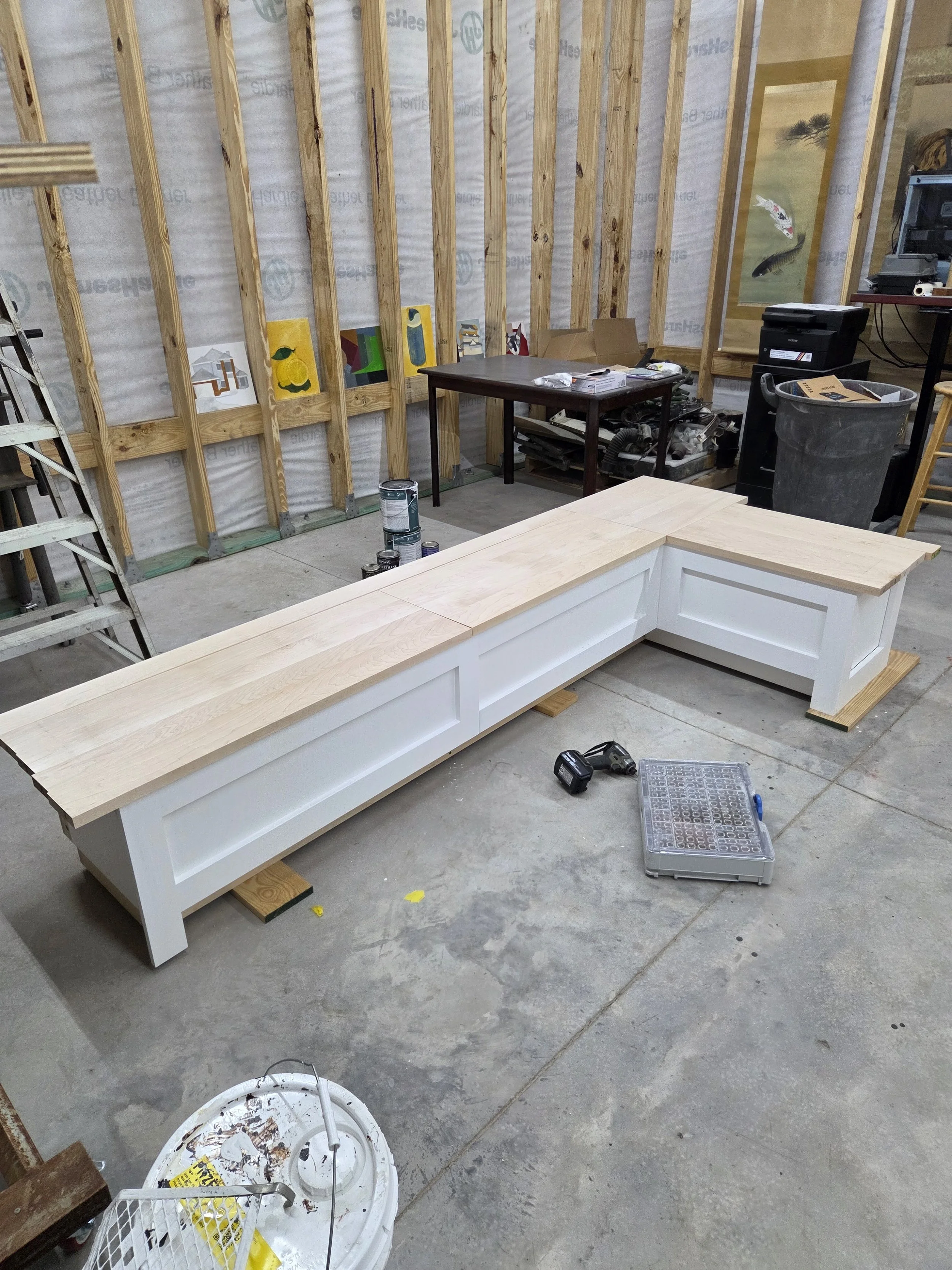 Room under construction with exposed wooden studs, a partially assembled white kitchen island, and tools scattered on the floor.