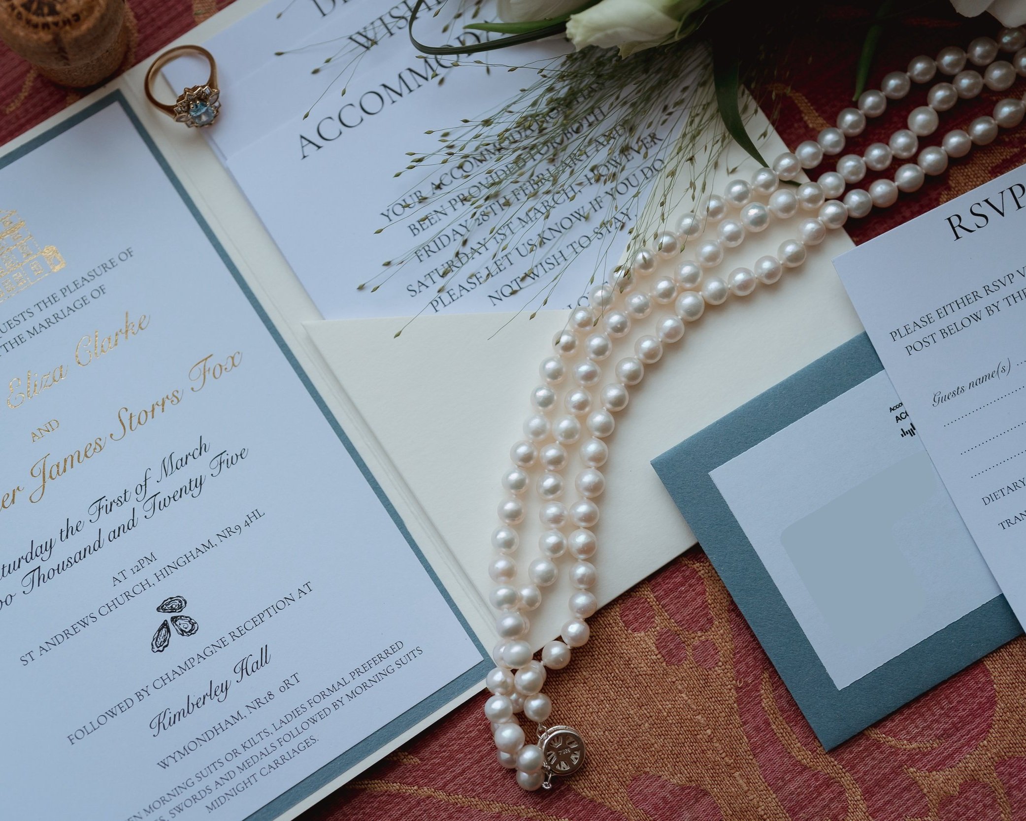 Flatlay of wedding invite, engagement ring and pearl necklace