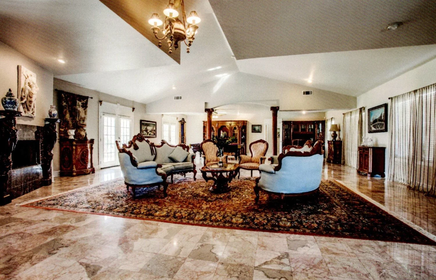 Spacious living room with vintage furniture, a large area rug, fireplace, and floor-to-ceiling curtains.