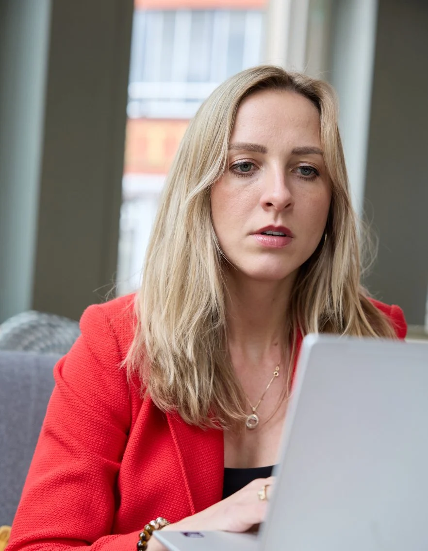 Vrouw in een rode jas kijkt geconcentreerd naar een laptop