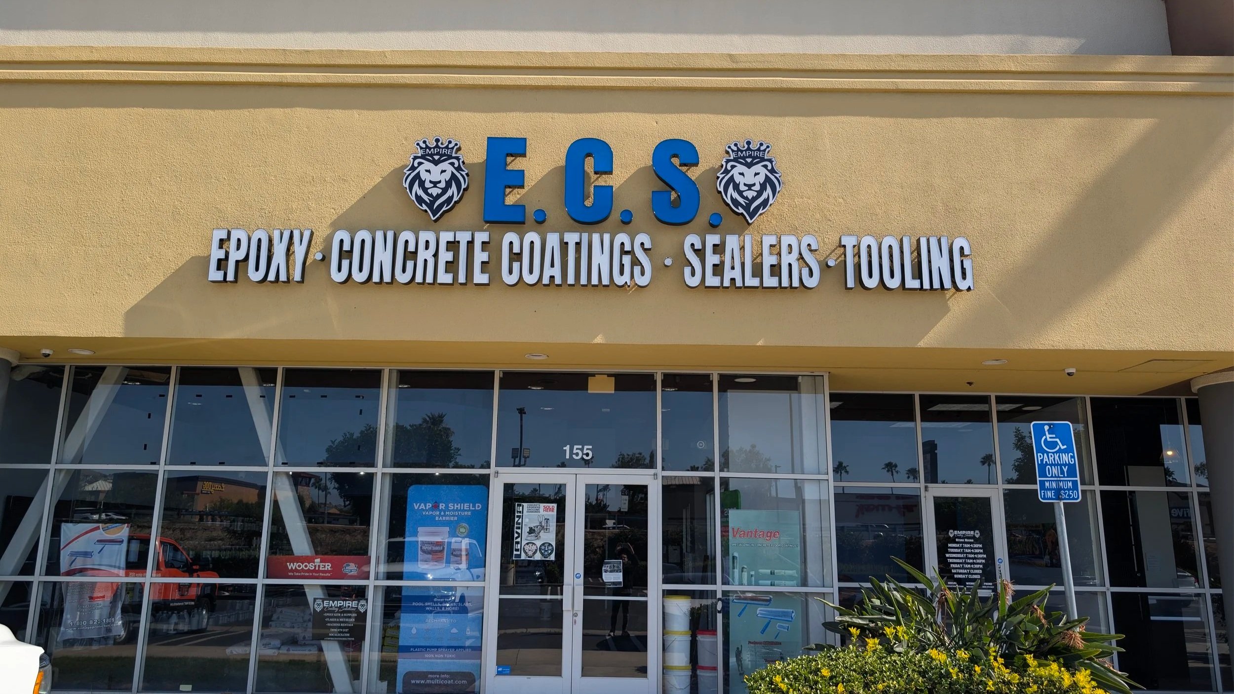 Storefront with signs reading E.C.S. and services like epoxy, concrete coatings, sealers, and tooling; logos with lion heads; parking sign for disabled