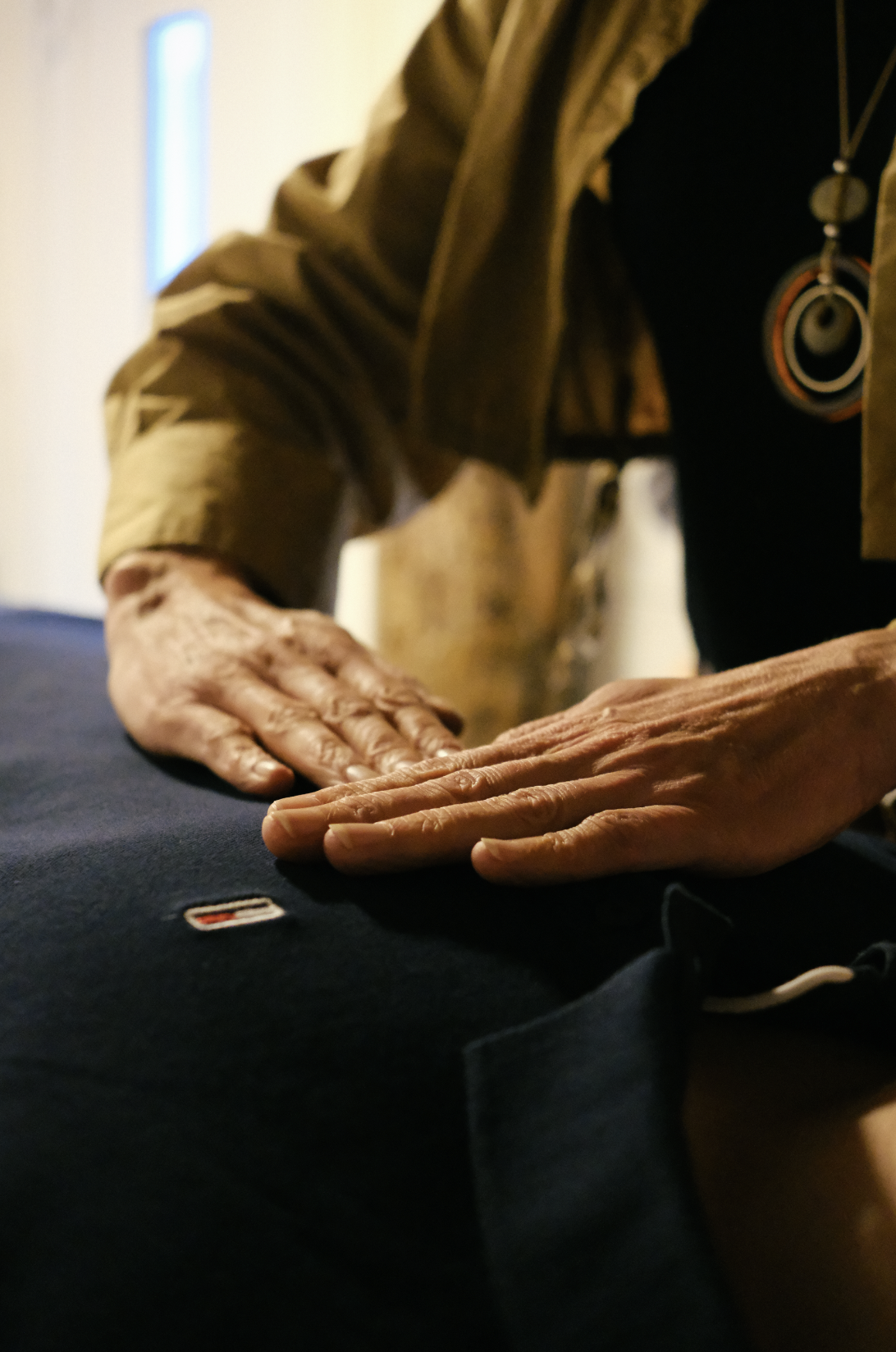 Mains de deux personnes posées sur une surface noire, une personne portant un collier avec un pendentif