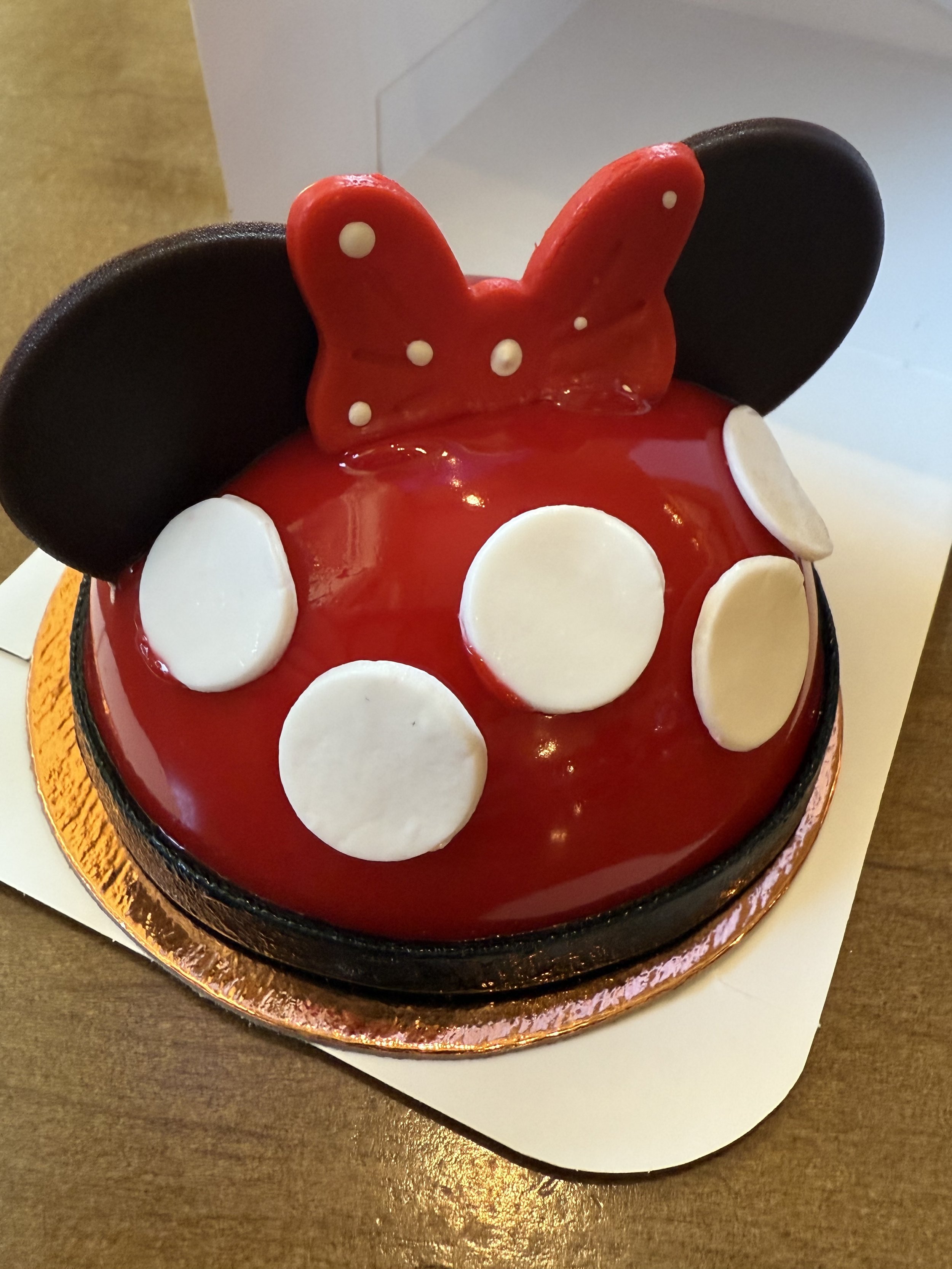 A dome-shaped cake decorated with a red and black theme, featuring large white polka dots and black circular shapes resembling ears, with a red bow on top. The design is reminiscent of a popular cartoon character.