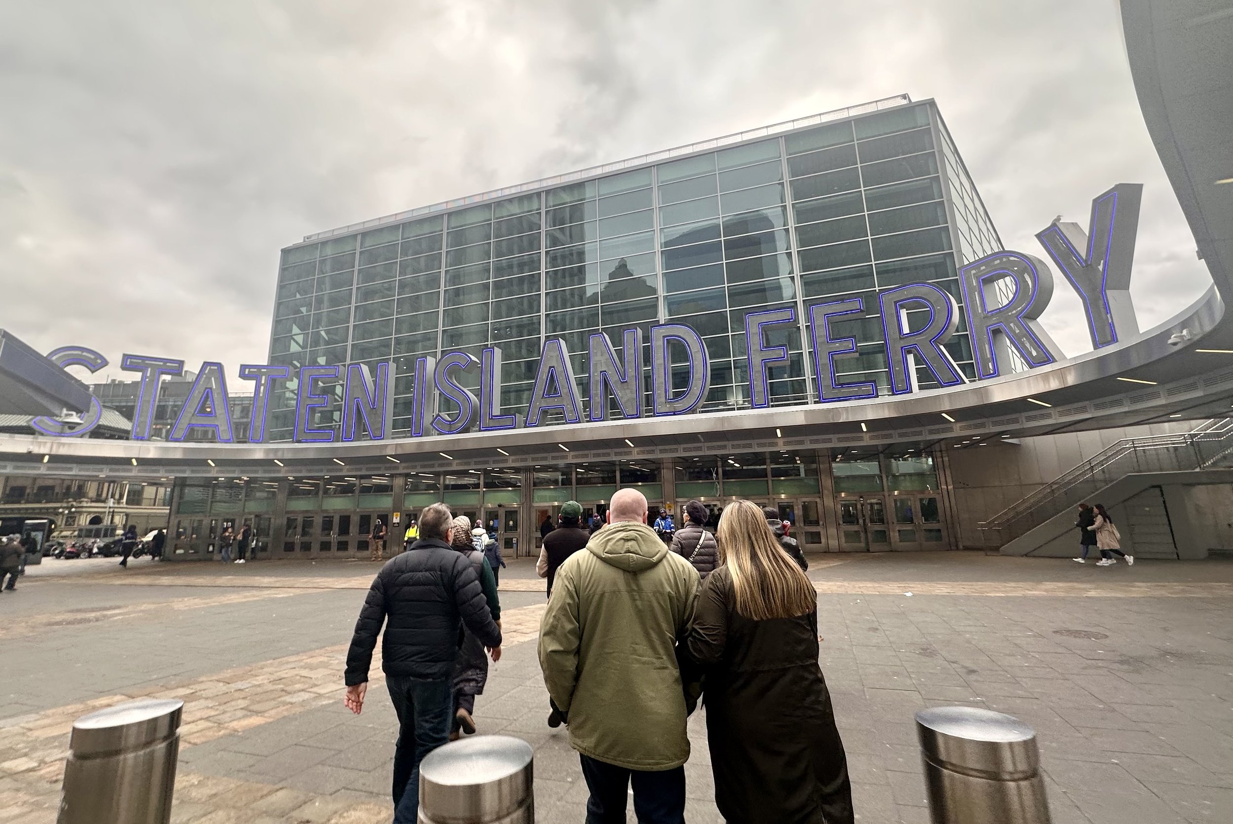 Entrance of Staten Island Ferry terminal with large signage and people walking towards it.