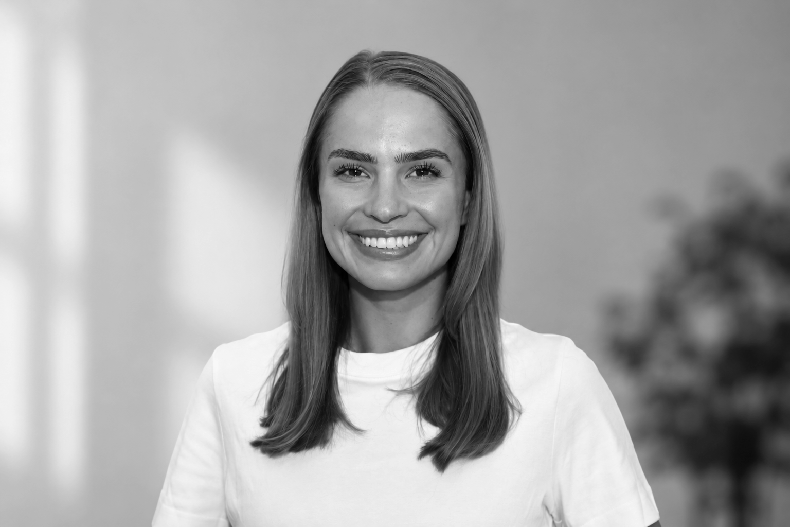 A young woman with long straight hair smiling in a black and white portrait, wearing a dark textured top.