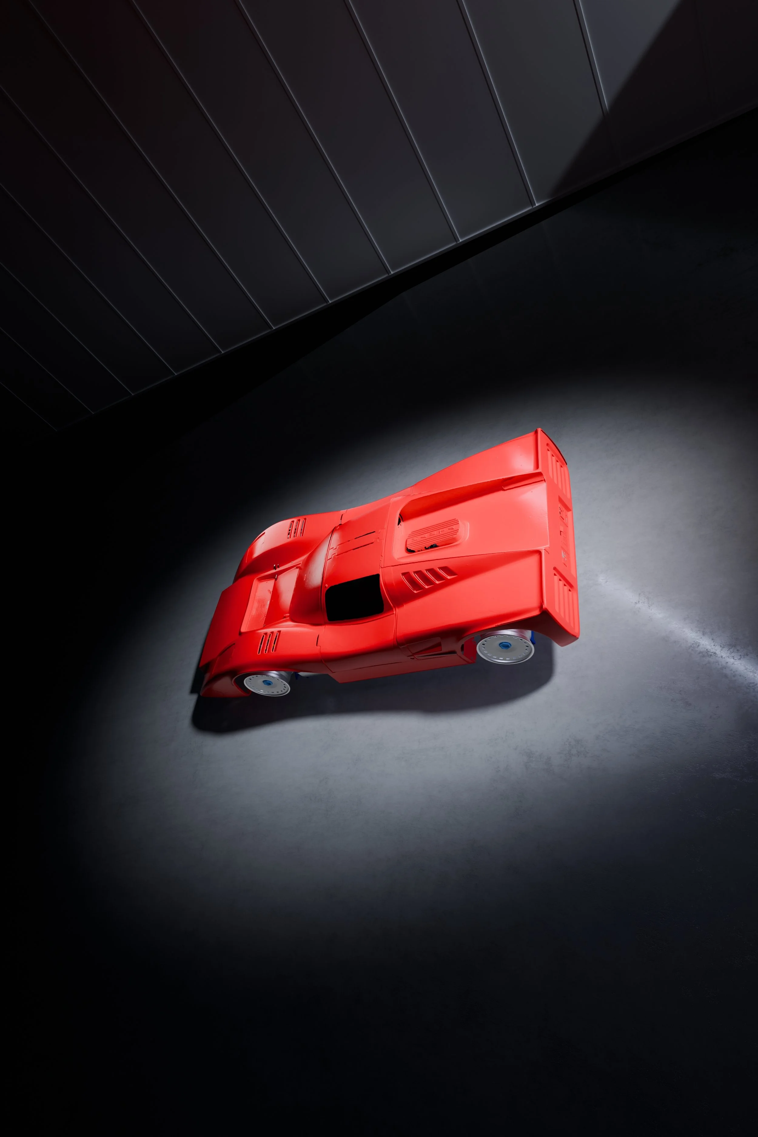 A red Manta Mirage race car on a gray surface in a dark room with a black background.