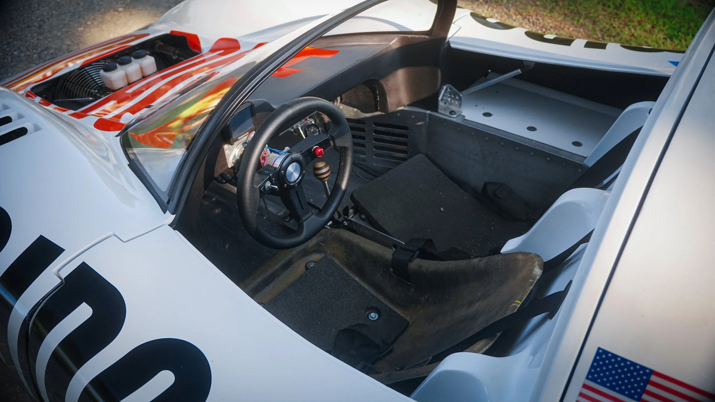 Interior of a race car showing a steering wheel, racing seat, and dashboard with minimal racing components.