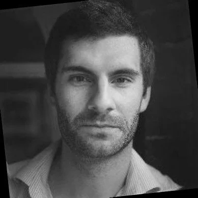Black-and-white portrait of a man with short dark hair and a beard, wearing a collared shirt.