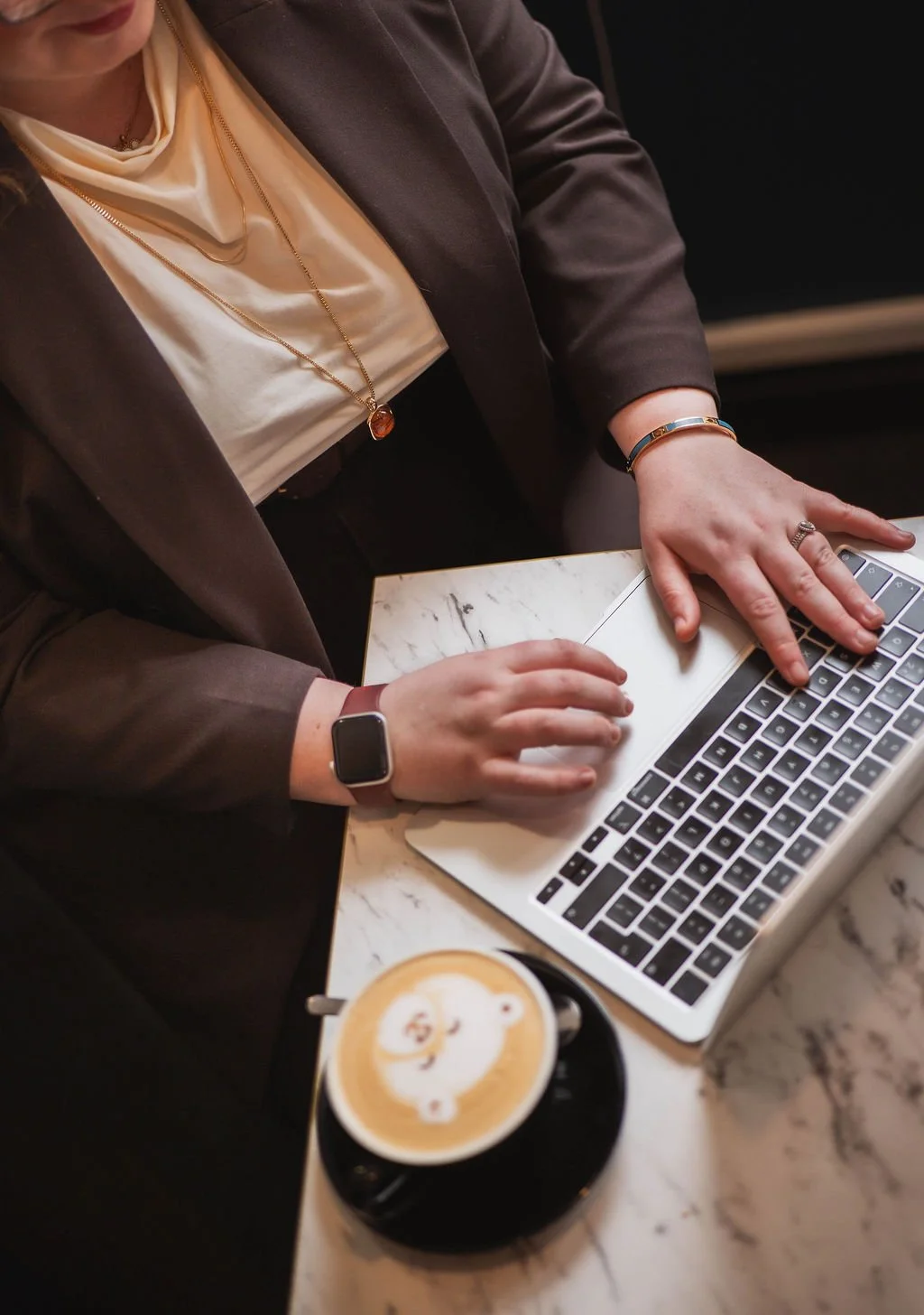 Person working on a laptop with a coffee drink on a marble table.