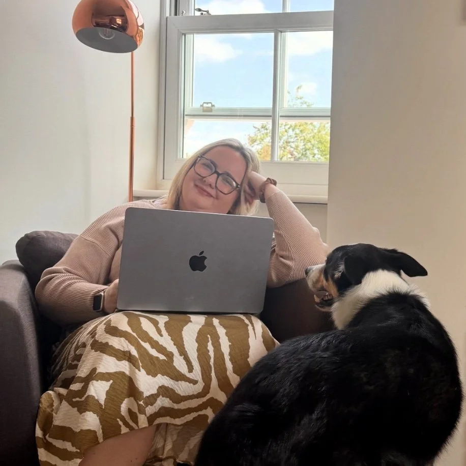 Abi smiling with her dog next to her, and laptop on lap