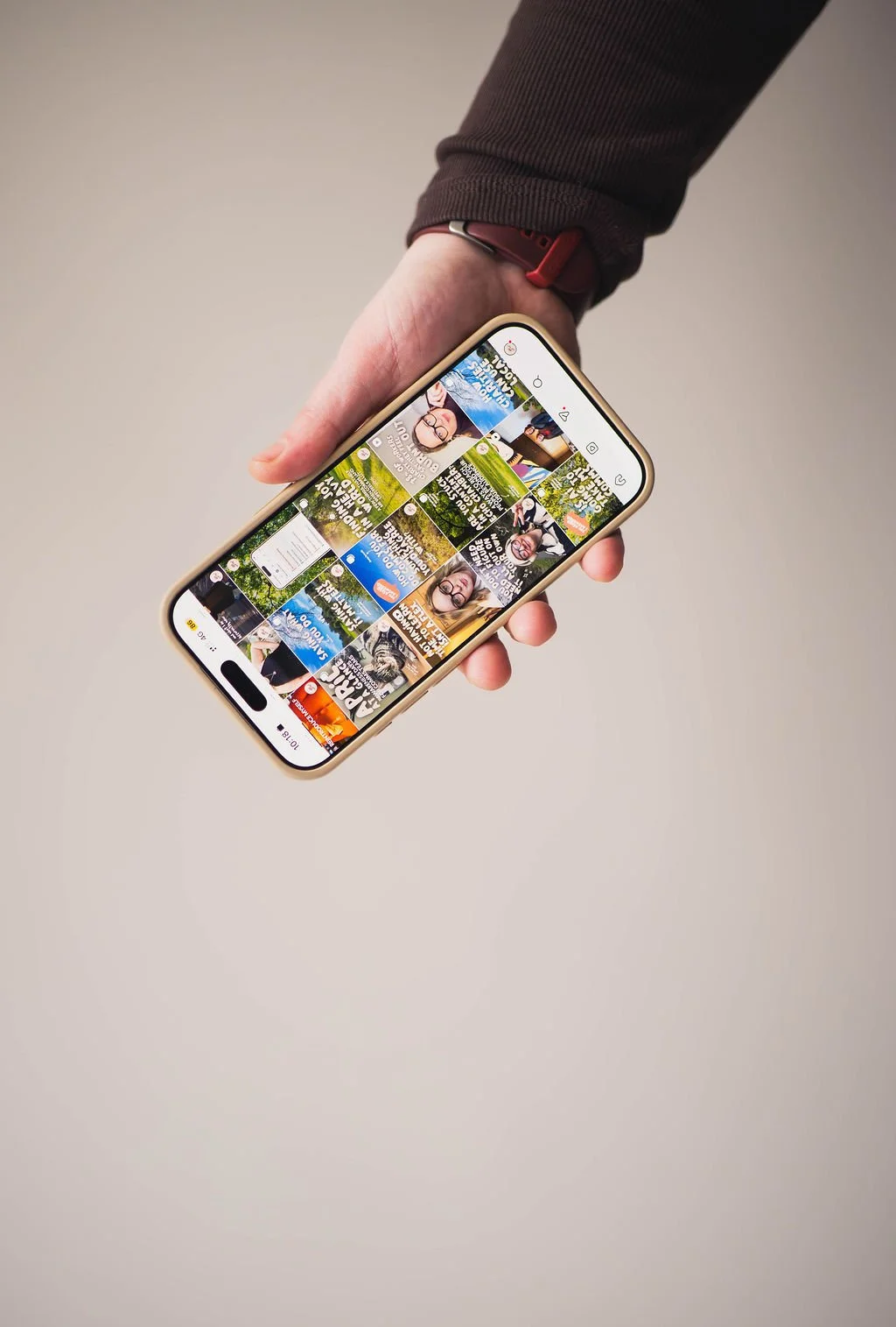A person holding a smartphone with a social media feed displayed on the screen, featuring various images and text.