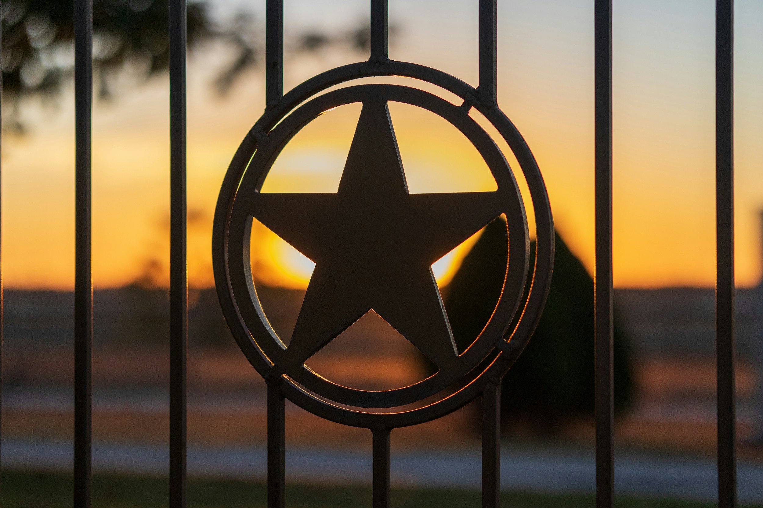 Black metal star emblem on a fence at sunset.