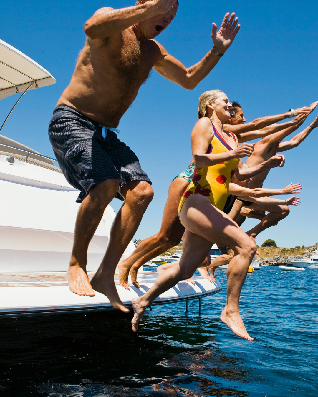 People jumping off a boat into water on a sunny day, holding arms out for balance.