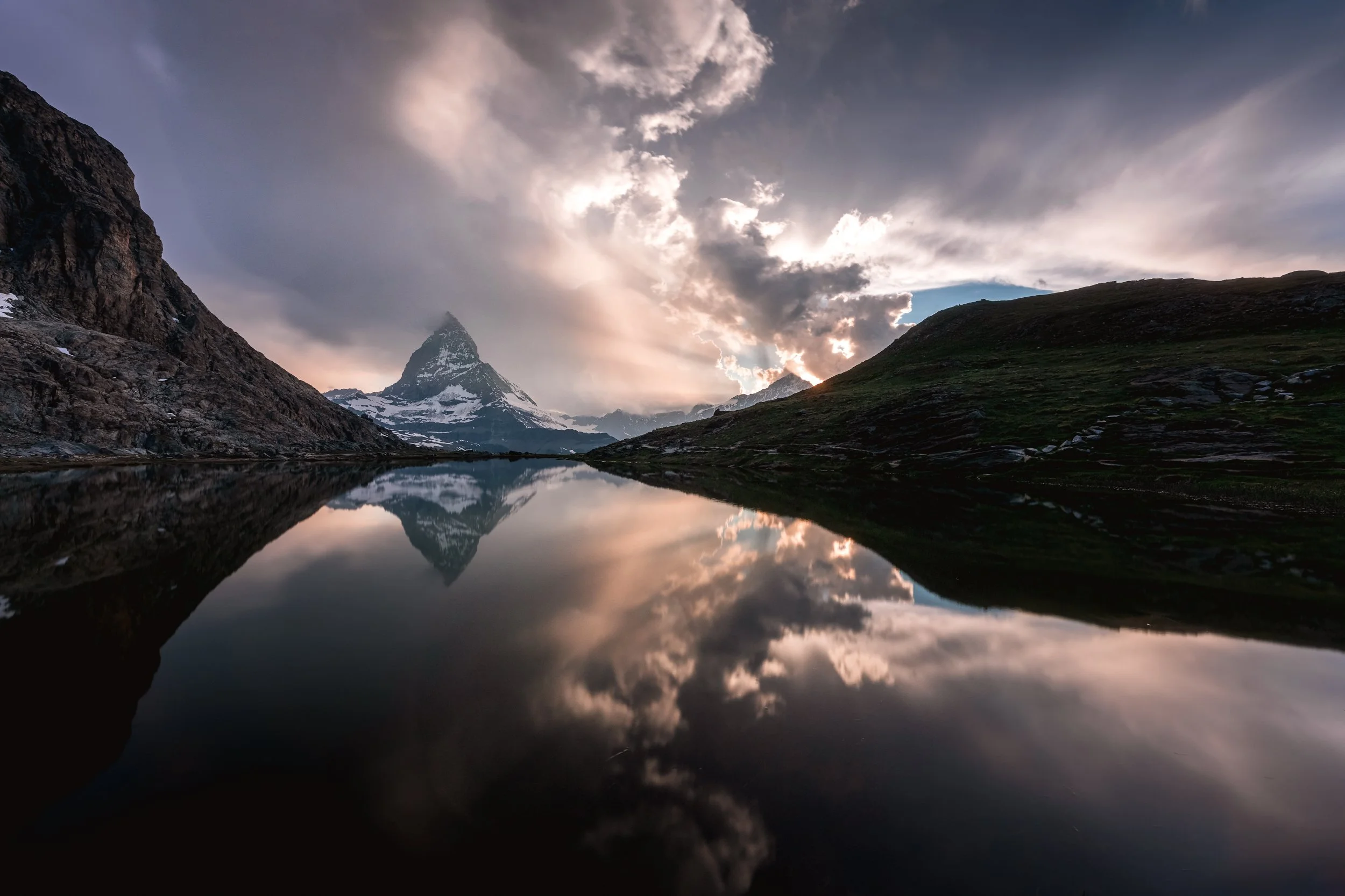 Snow-capped mountain reflected in a calm lake with dramatic cloudy sky at sunset