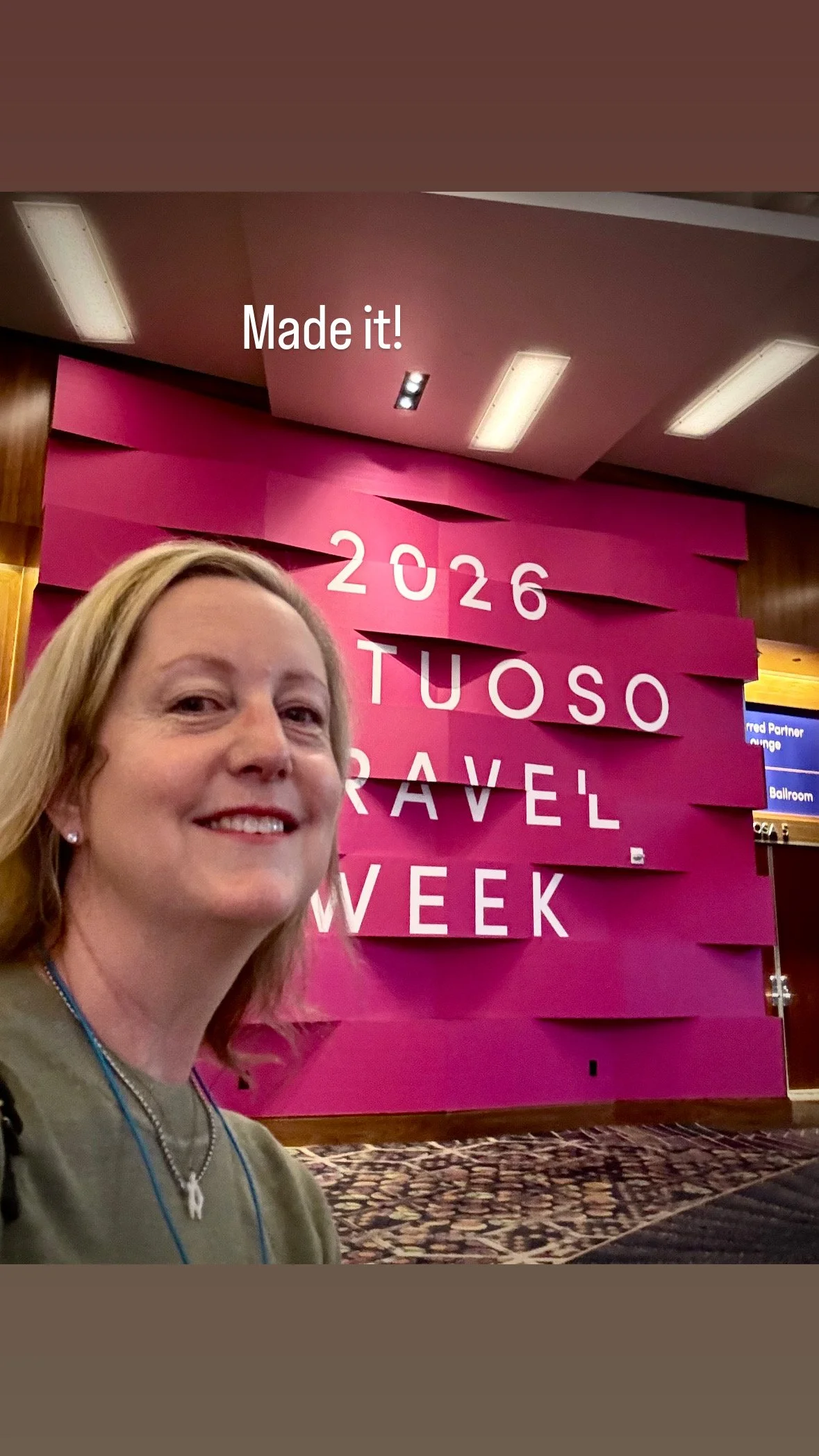 Melissa taking a selfie at an event, with a pink sign in the background that reads '2026 VIRTUOSO TRAVEL WEEK'