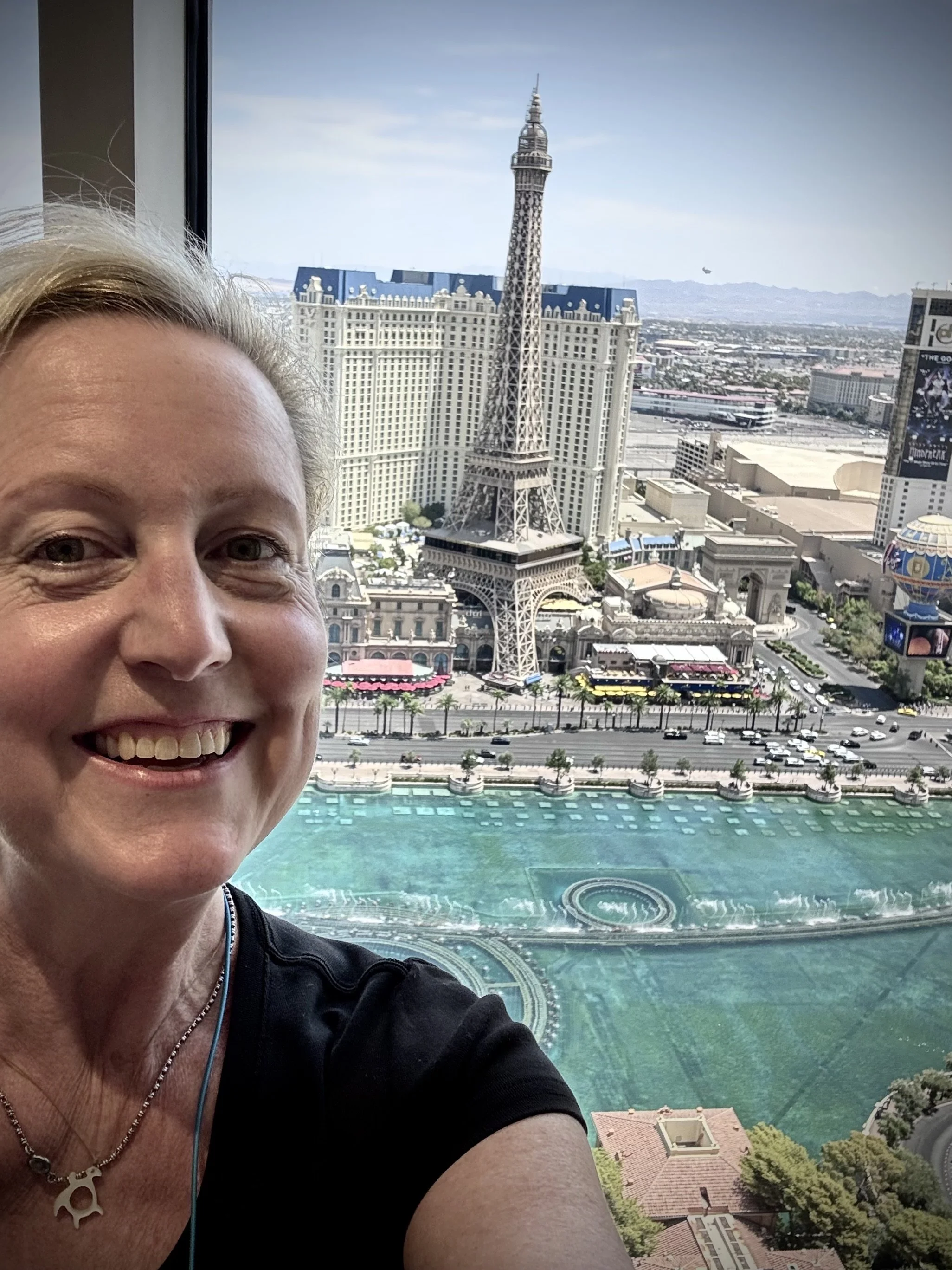 Melissa taking a selfie in from the Bellagio in Las Vegas, with the replica Eiffel Tower and other buildings in the background.