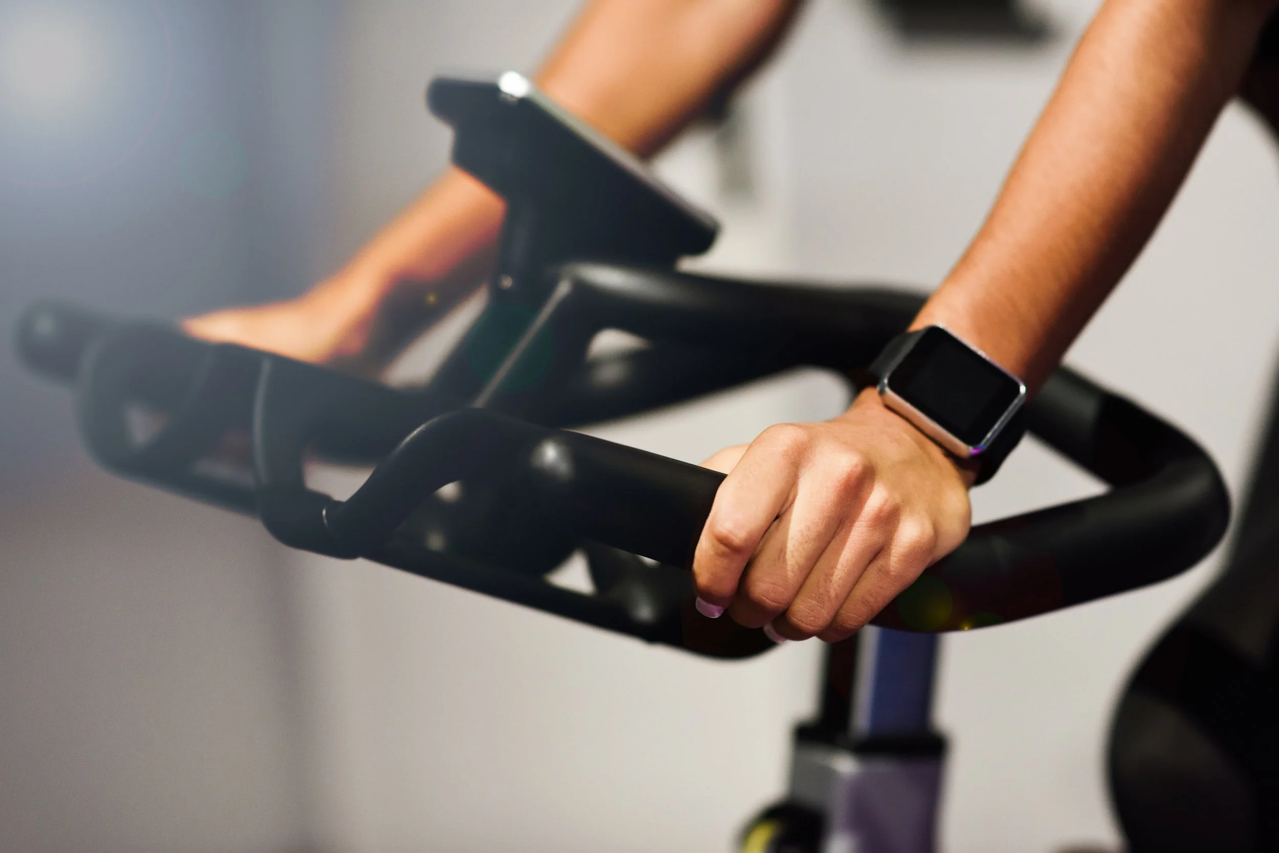 Person using exercise bike wearing smartwatch, focus on handlebars and hands.