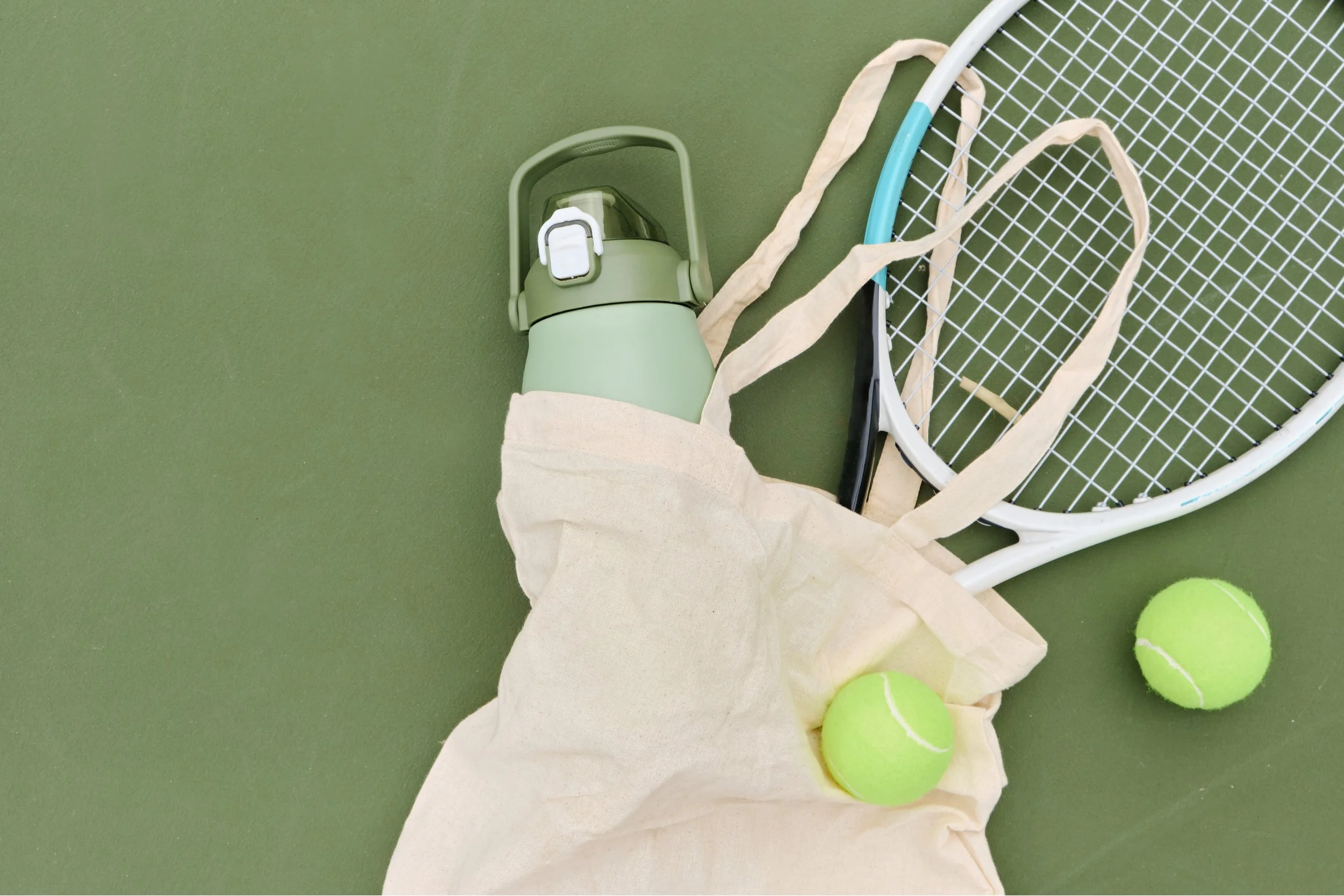 Tennis racket, balls, water bottle, and canvas bag on green surface
