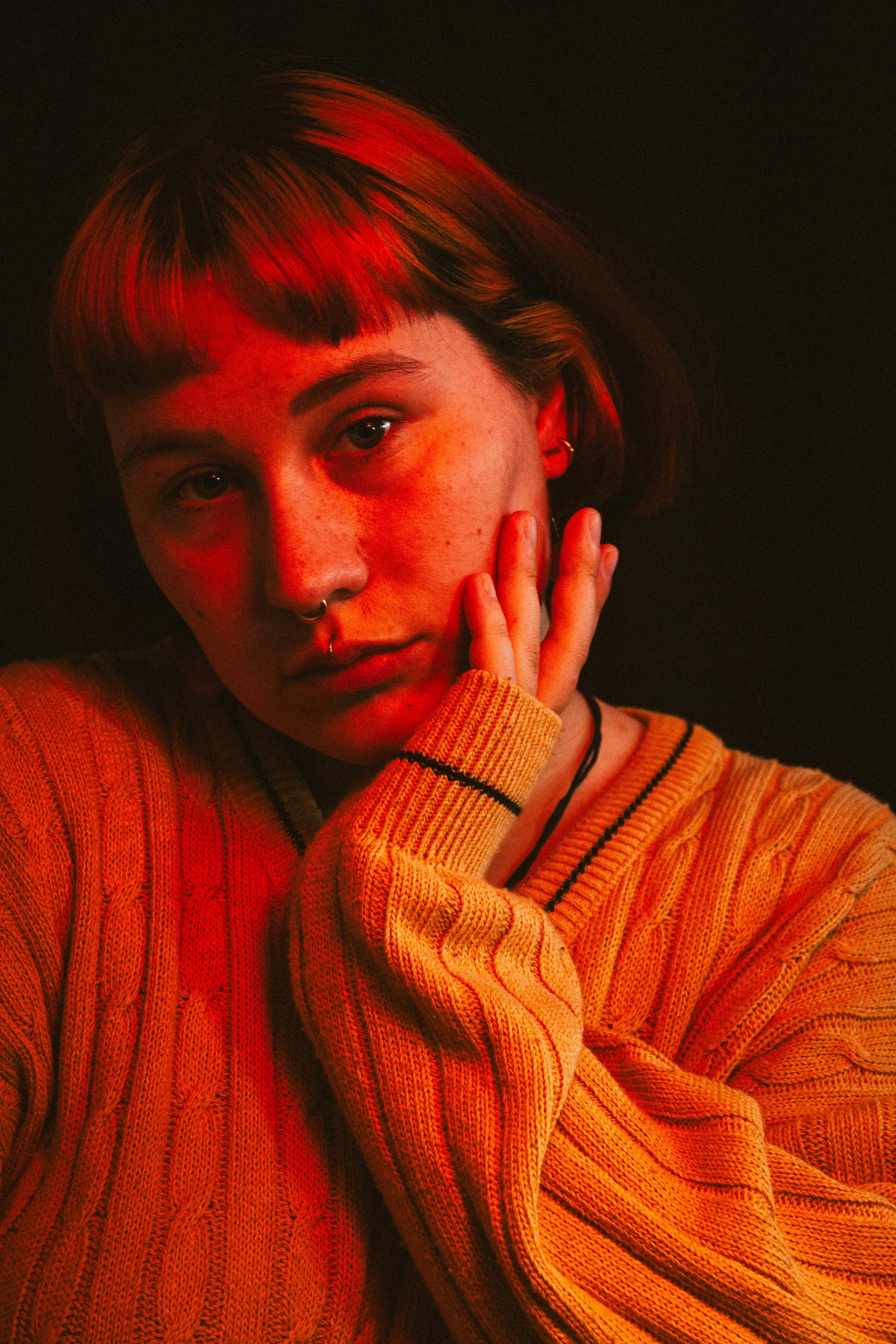 Porträt von Julia mit einem gelben Strick-Pullover in einem orange-rötlichem Studio-Setting.