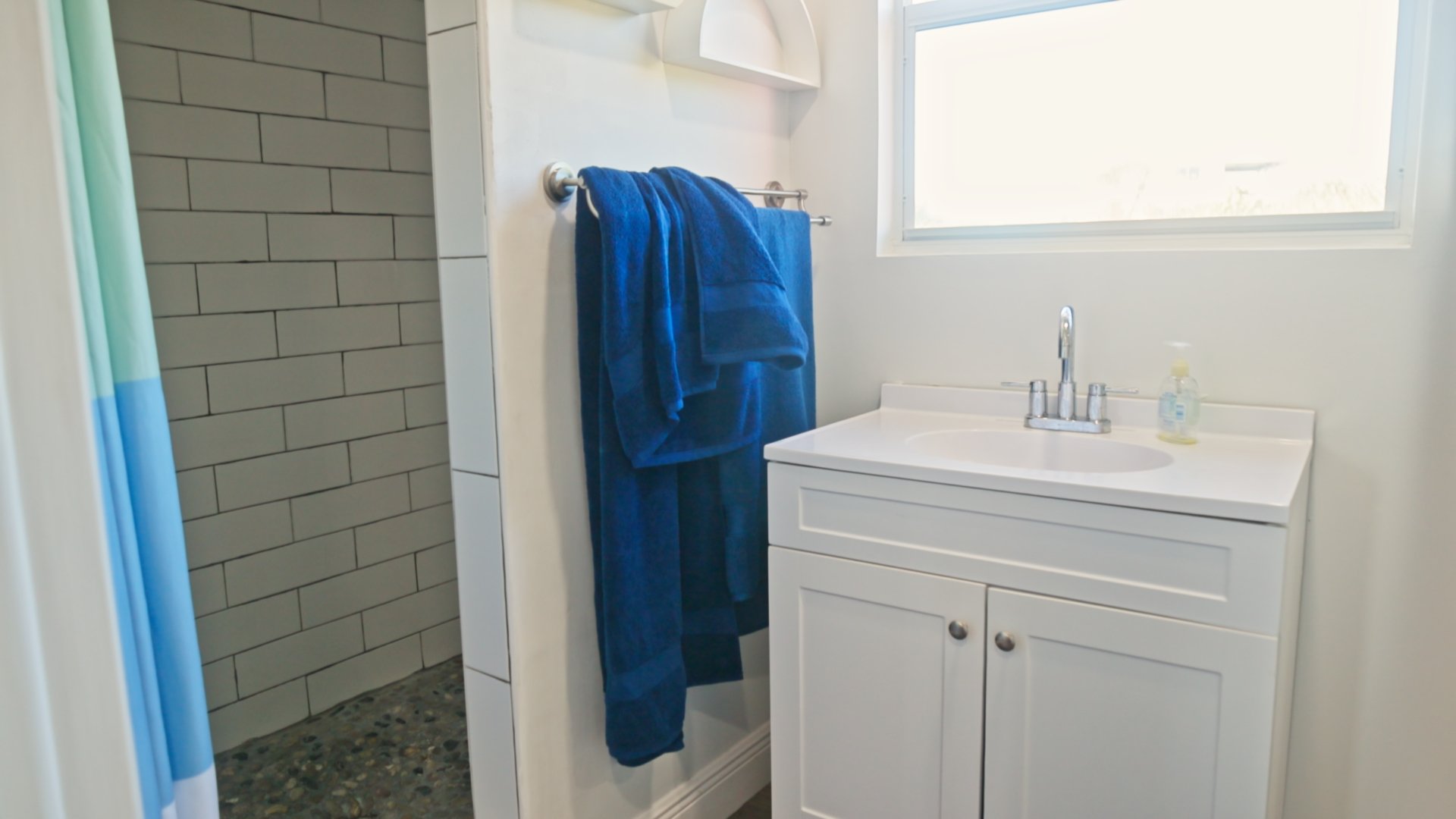 Small modern bathroom with shower, vanity, and blue towel inside B Happy Beach House.