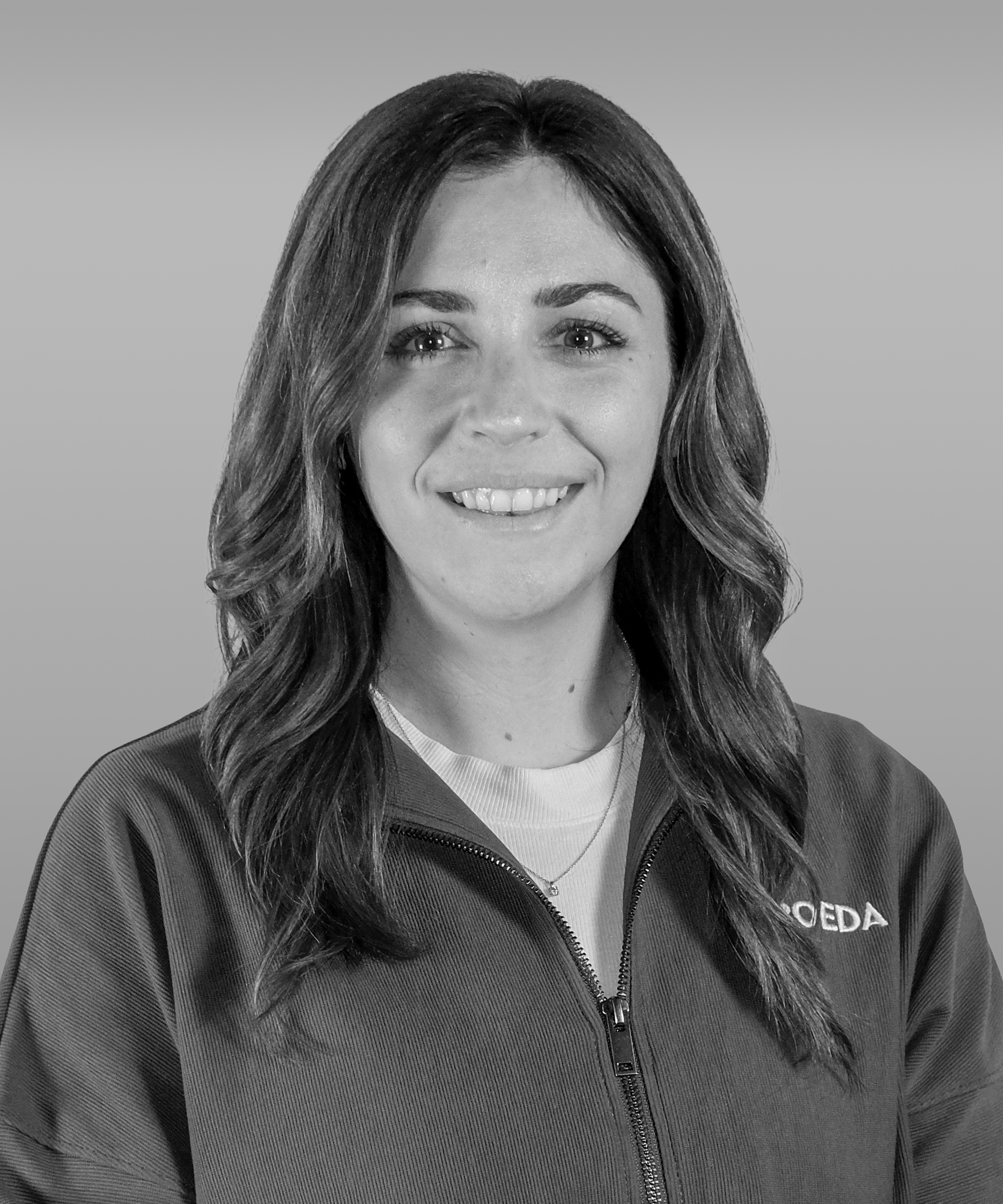 Black and white portrait of a smiling woman with shoulder-length wavy hair wearing a zip-up jacket.