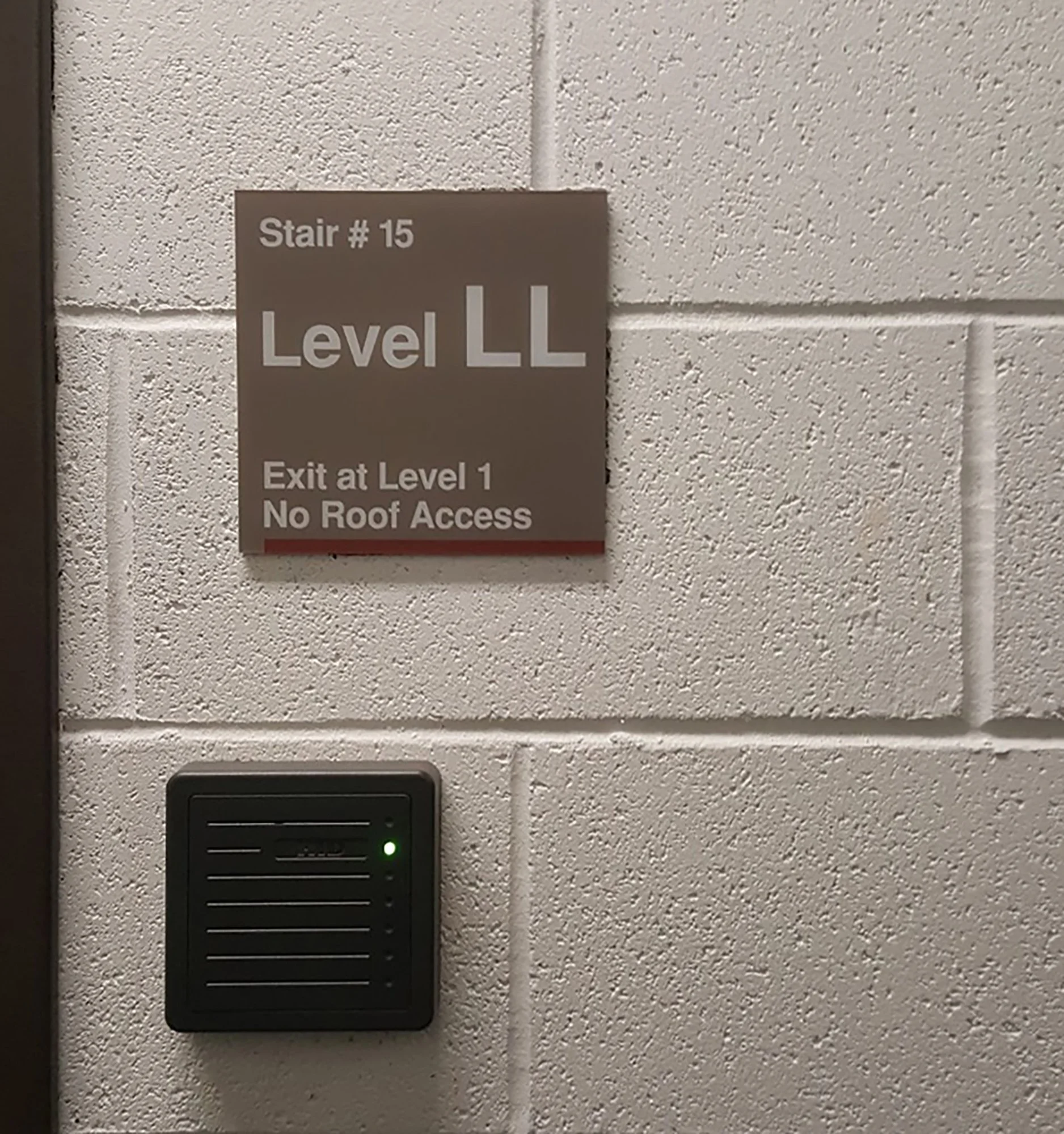 Sign indicating Stair #15 at Level LL with exit at Level 1 and no roof access, next to a wall-mounted access control device with a green light.