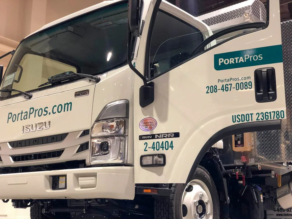 Front section of a white Isuzu PortaPros delivery truck with company branding and contact information on the door.