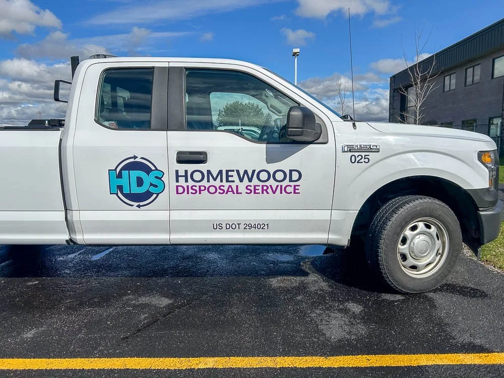 A white pickup truck with a logo and text for Homewood Disposal Service parked in a lot.