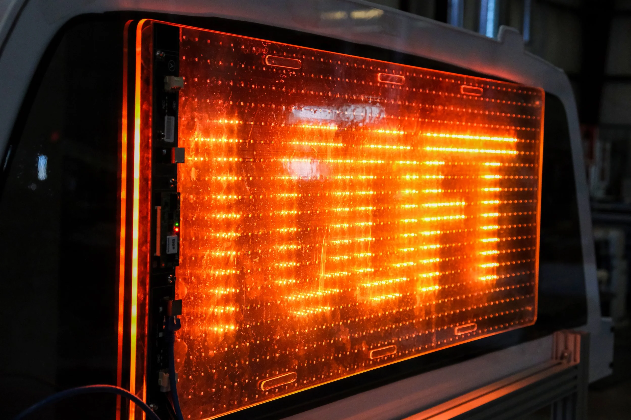 A close-up view of a large electronic display panel with orange and red lights arranged in horizontal rows, reflecting and creating a glowing pattern.