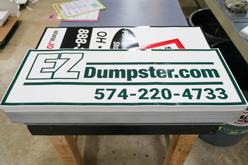 A stack of EZ Dumpster.com stickers with a green logo and contact number on a workbench.