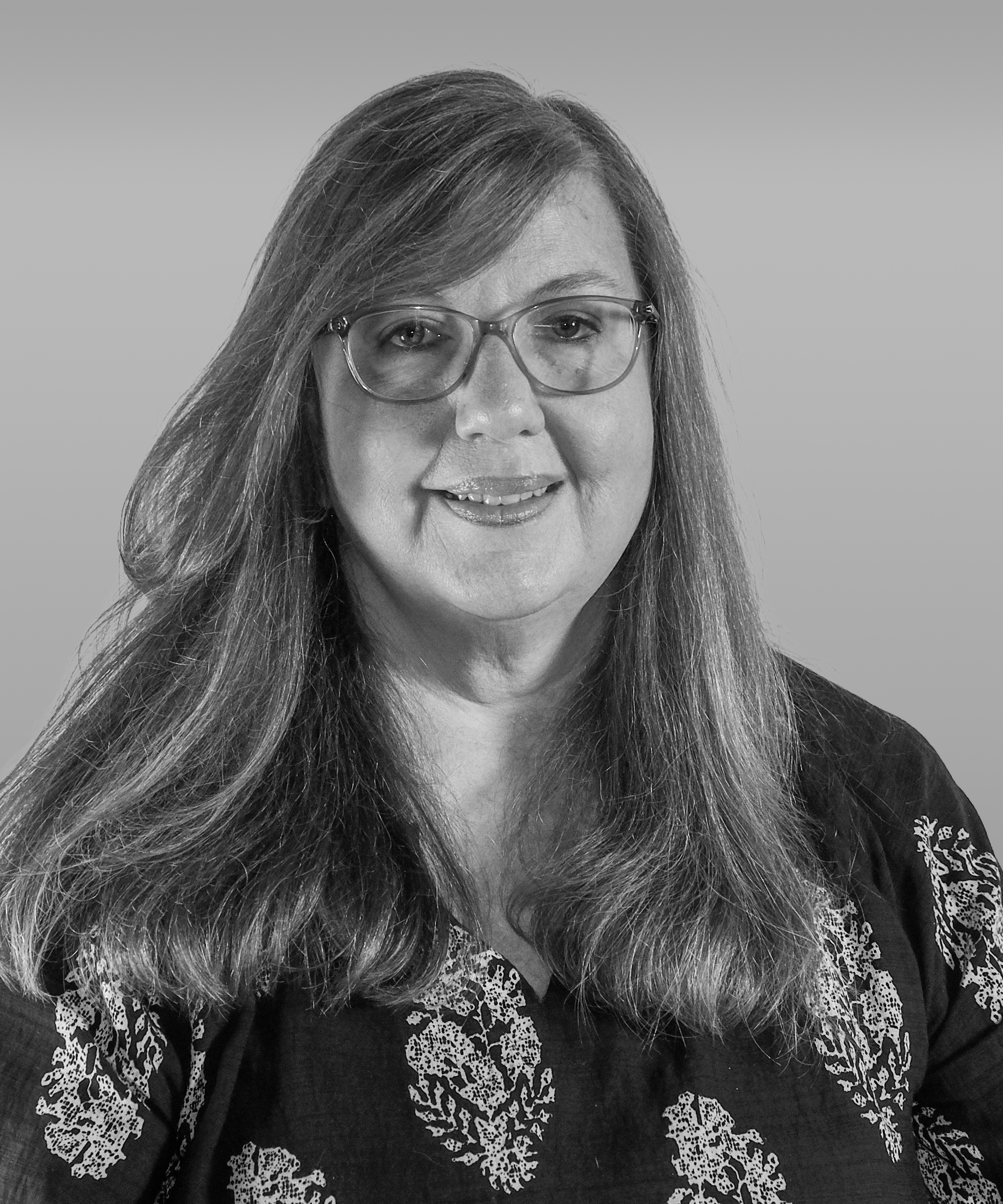 Black and white portrait of a woman with glasses, shoulder-length hair, wearing a dark top with lace-like pattern, smiling slightly.