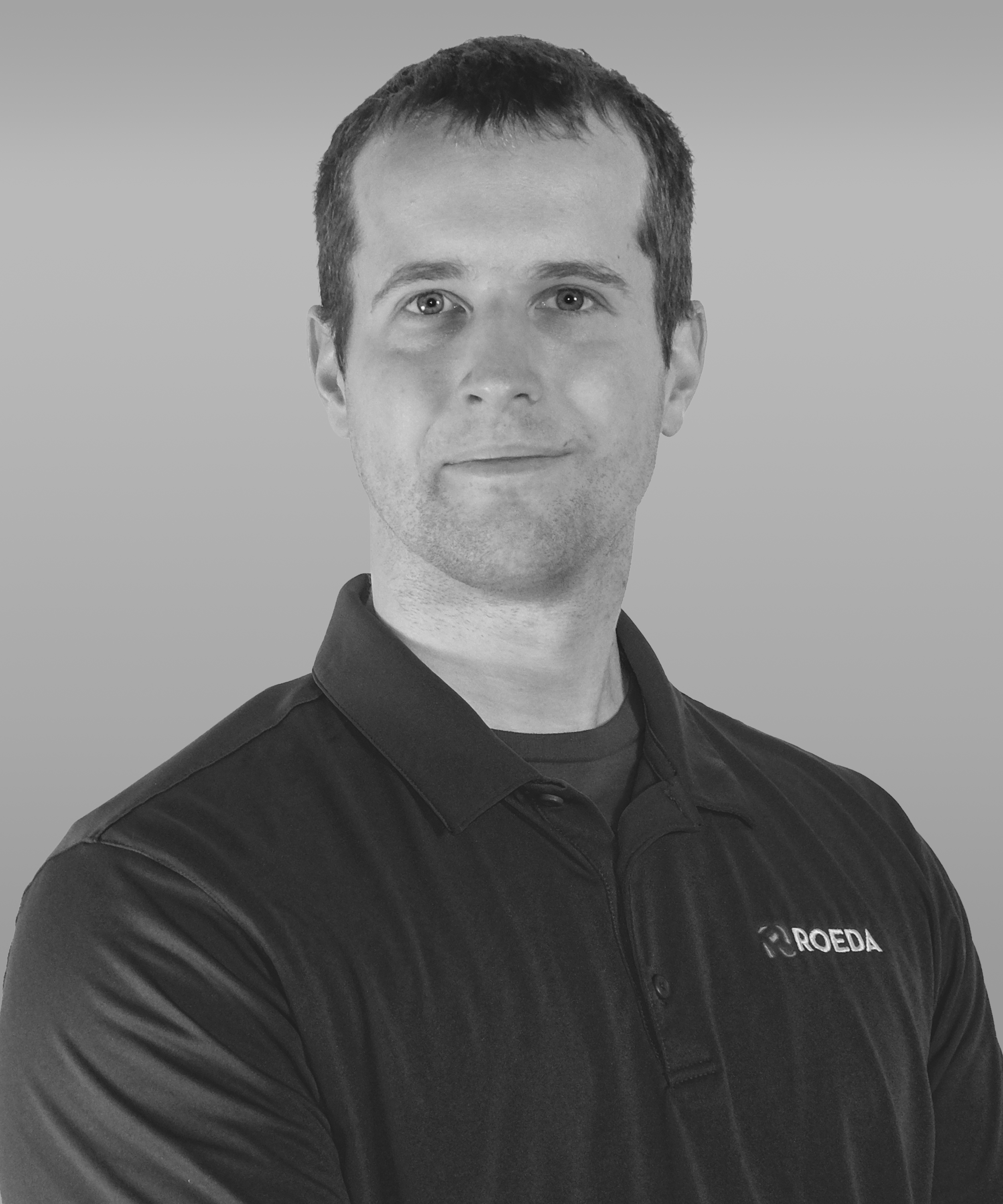 Black and white portrait of a man wearing a collared shirt with the logo 'ROEDA' on it, looking directly at the camera with a neutral expression.