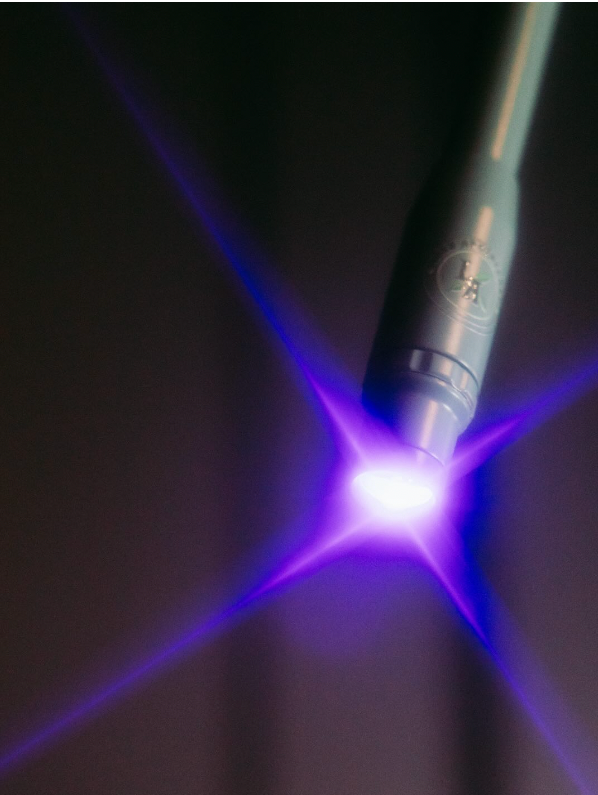 Close-up of a laser pen emitting purple light and creating star-shaped light rays against a dark background.