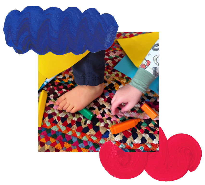 child hand and feet over a colorful rug with some colored markers and paper.