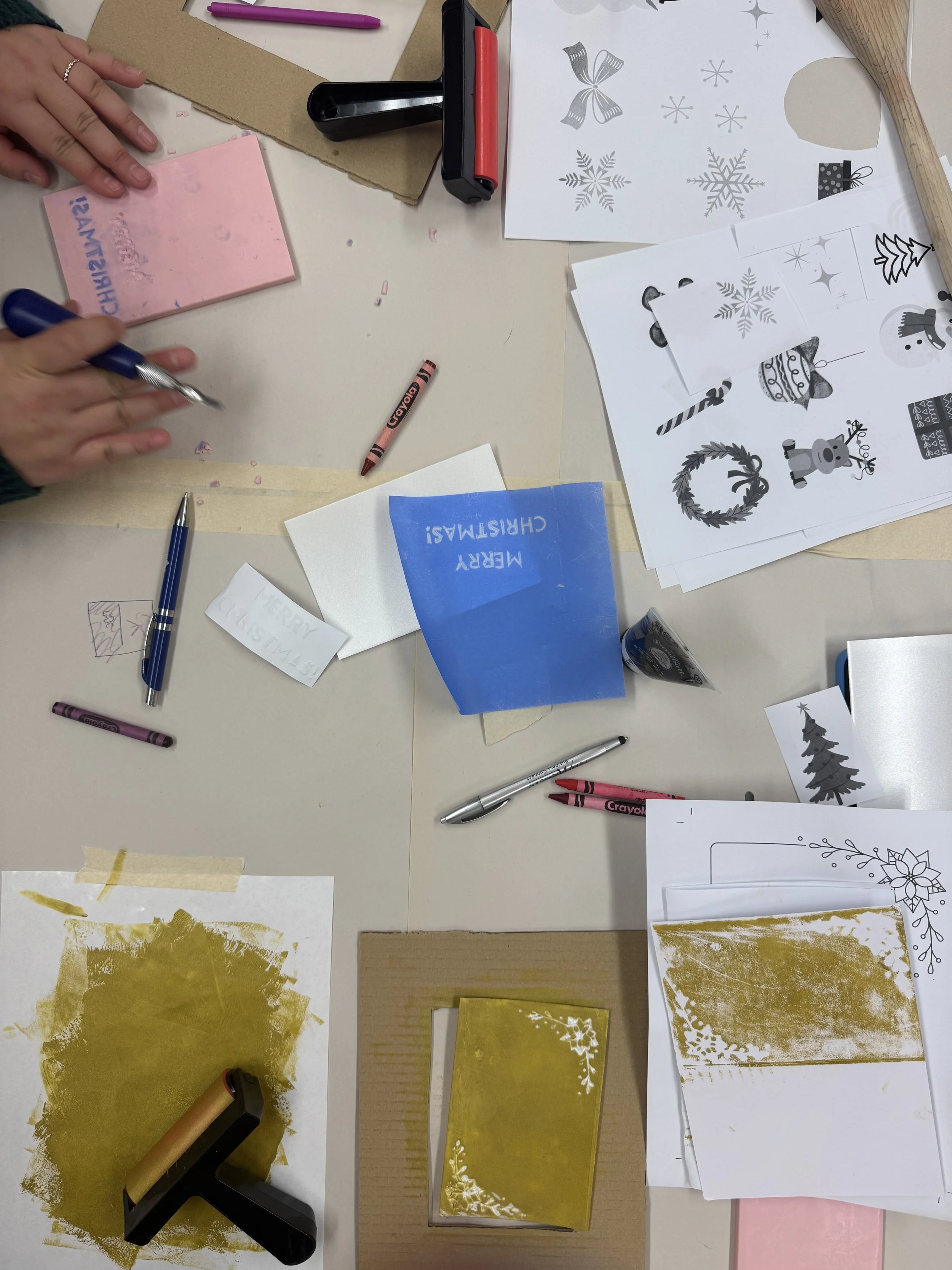 A table with various holiday craft supplies, including paper, stamps, ink pads, pens, scissors, and templates for making holiday decorations.