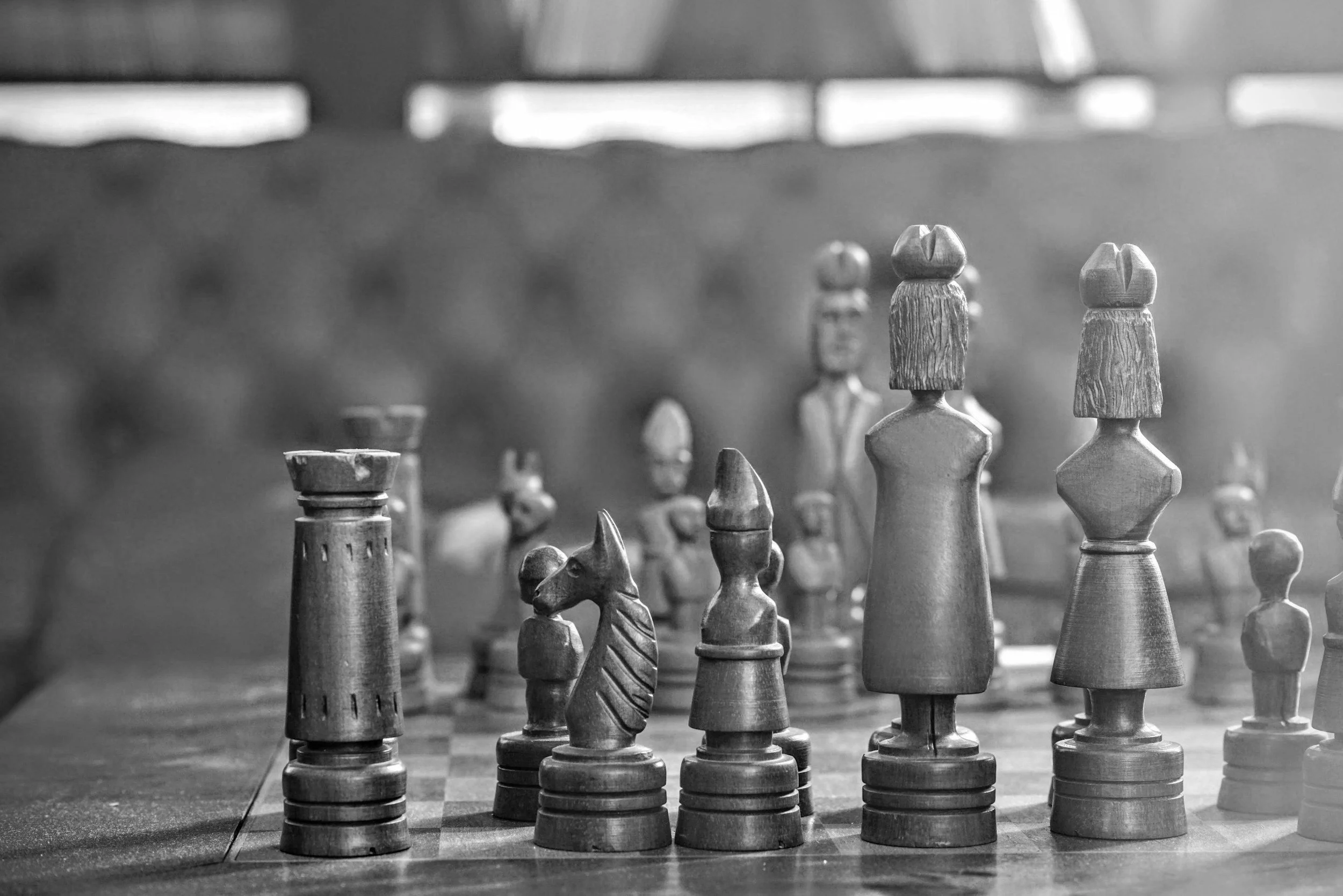 Black and white photo of wooden chess pieces arranged on a chessboard.