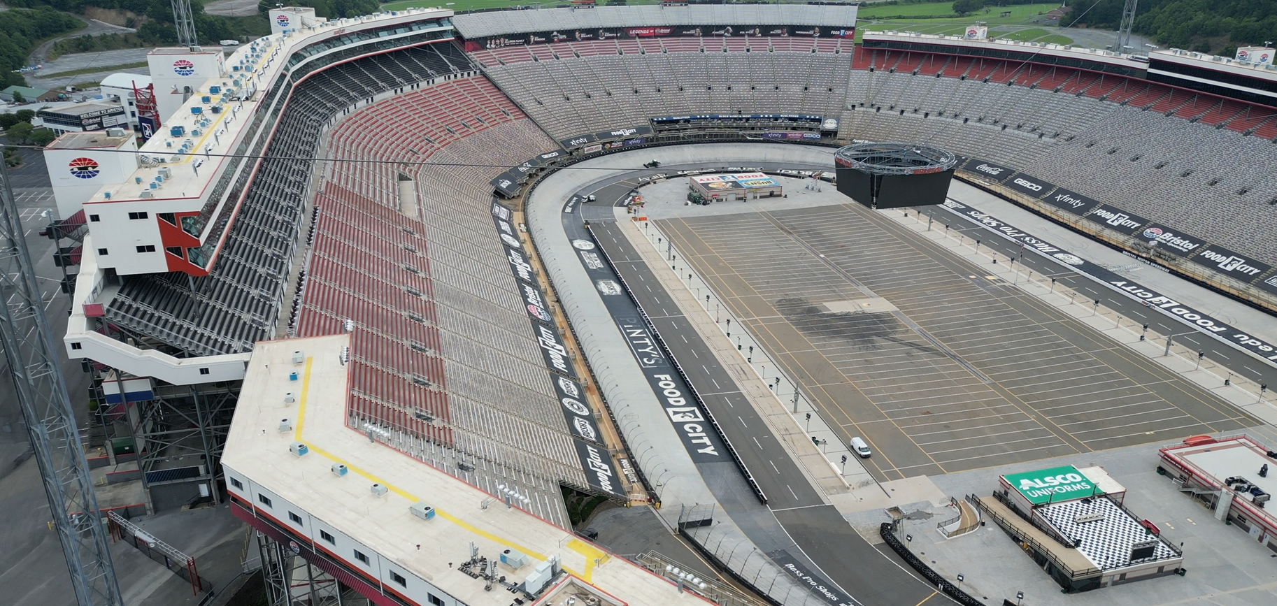 Empty NASCAR stadium with a large racing track, bleachers, and a digital screen, during daytime.