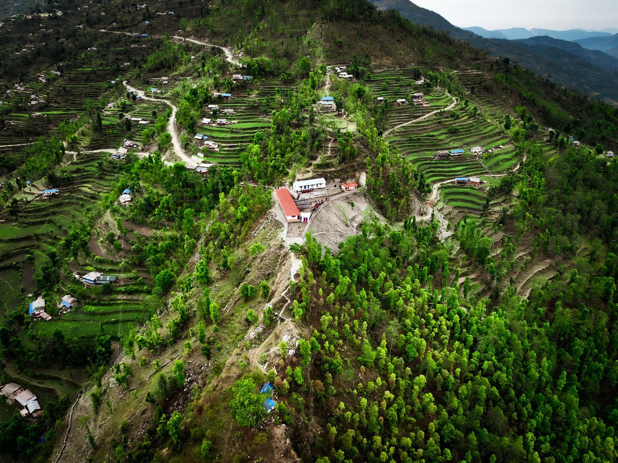 Aerial view of terraced rice fields and small houses on a lush green hillside in a mountainous region.