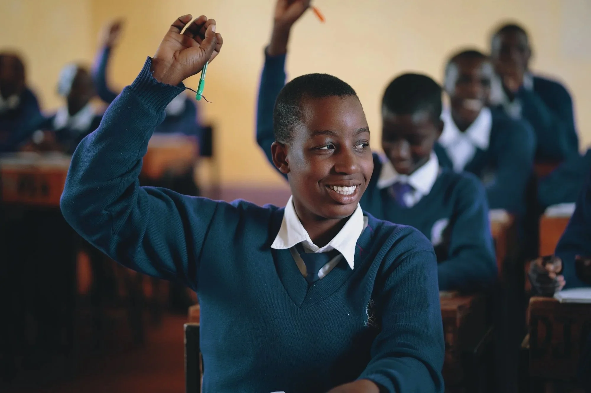 Five children and one adult sitting in a circle outdoors in a grassy area with trees and a fence in the background.