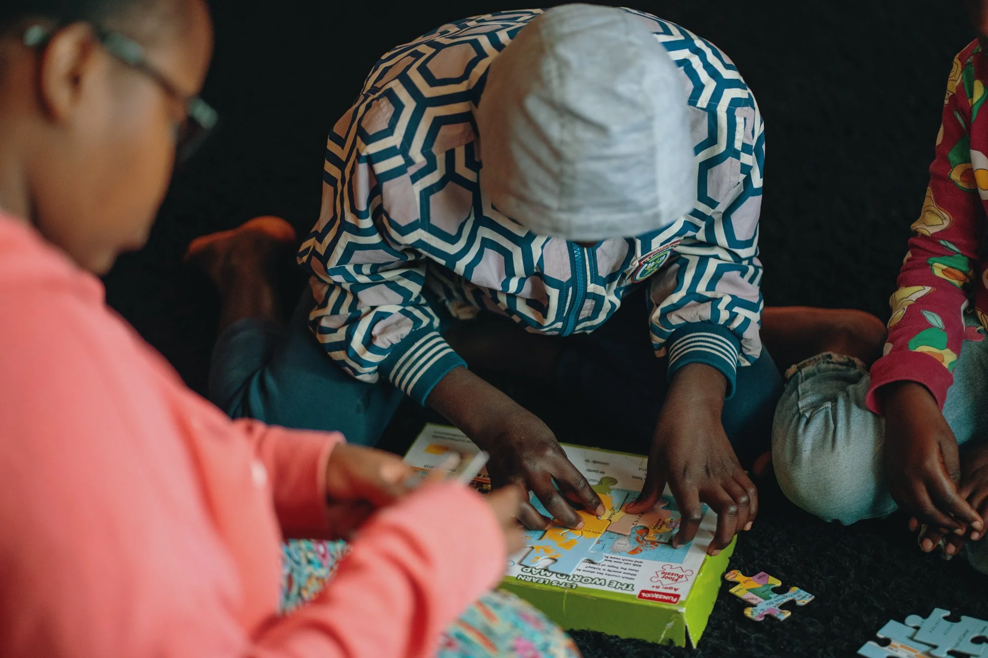 A woman and a young girl smiling outdoors, with the girl wearing a plaid dress and carrying a shoulder bag.
