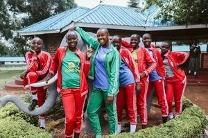 A group of young students in red school uniforms standing outdoors with a teacher.