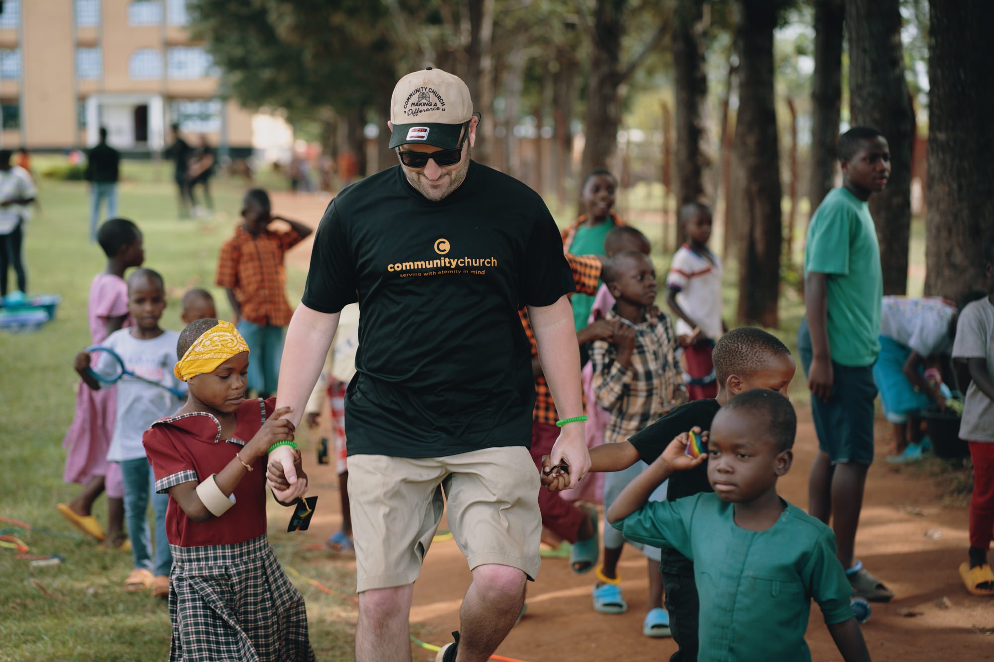 Group of women and girls posing outdoors in front of a sign for the Tarime School of Nursing, smiling and sitting or standing together.